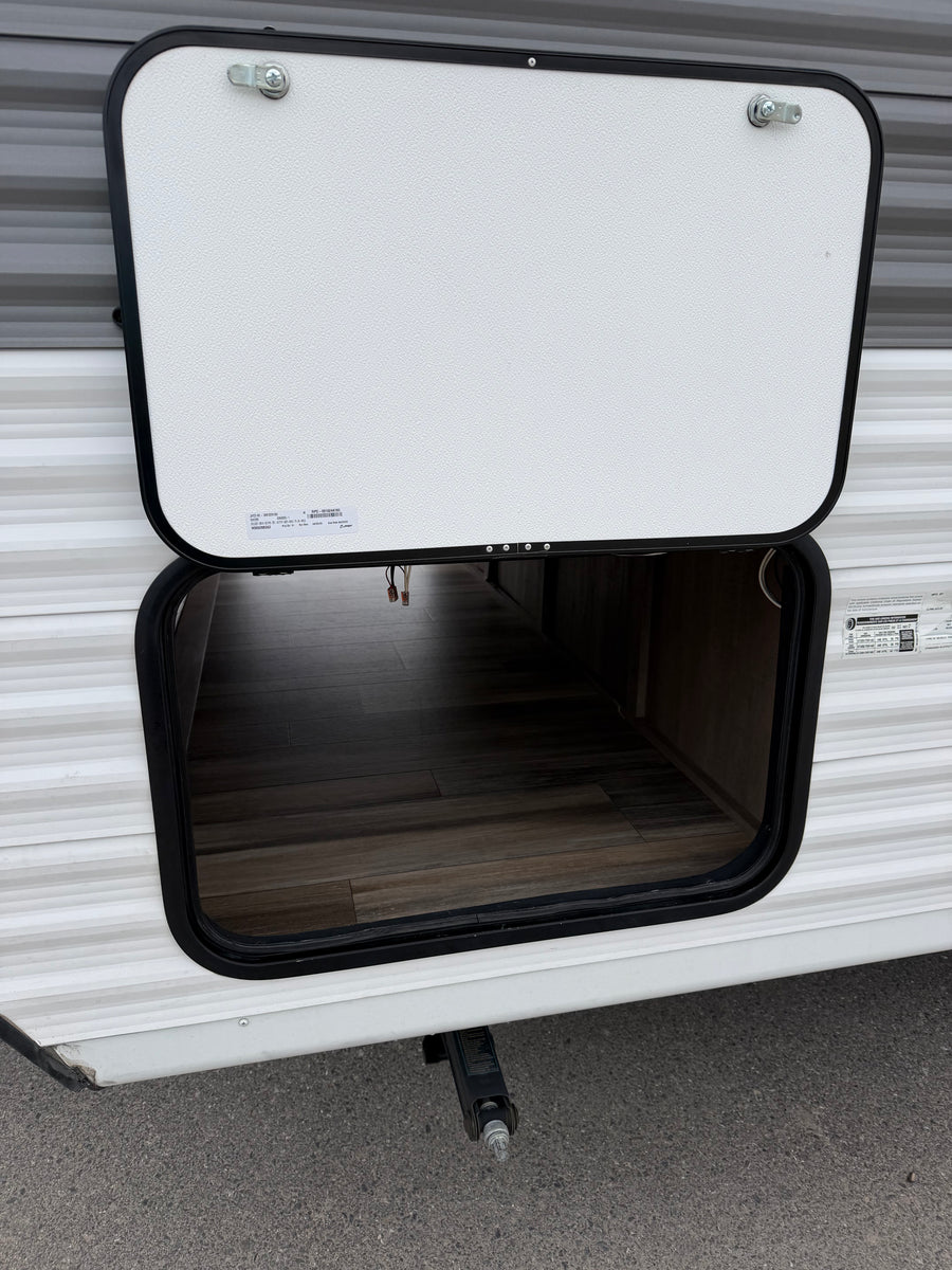 Open exterior storage compartment on an RV rental, revealing a wood-look floor. A leveling jack is seen below.