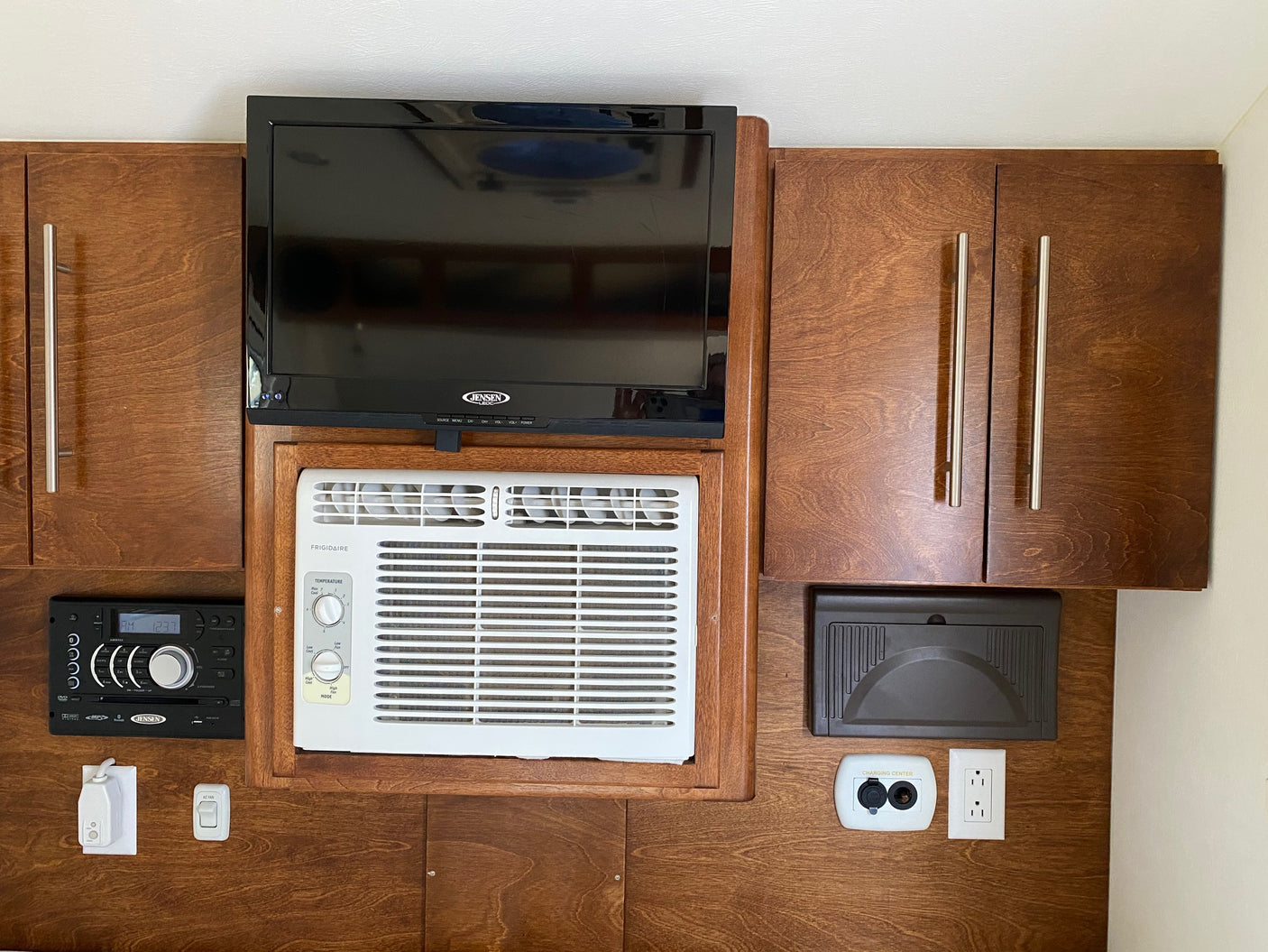 RV rental interior setup: compact TV, AC unit, stereo, and power outlets integrated into sleek wooden cabinetry.