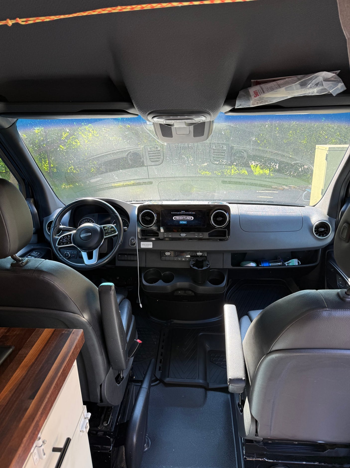 and seats. Frosty windshield shows a snowy exterior.|RV rental camper van interior featuring a cozy bed with colorful bedding
