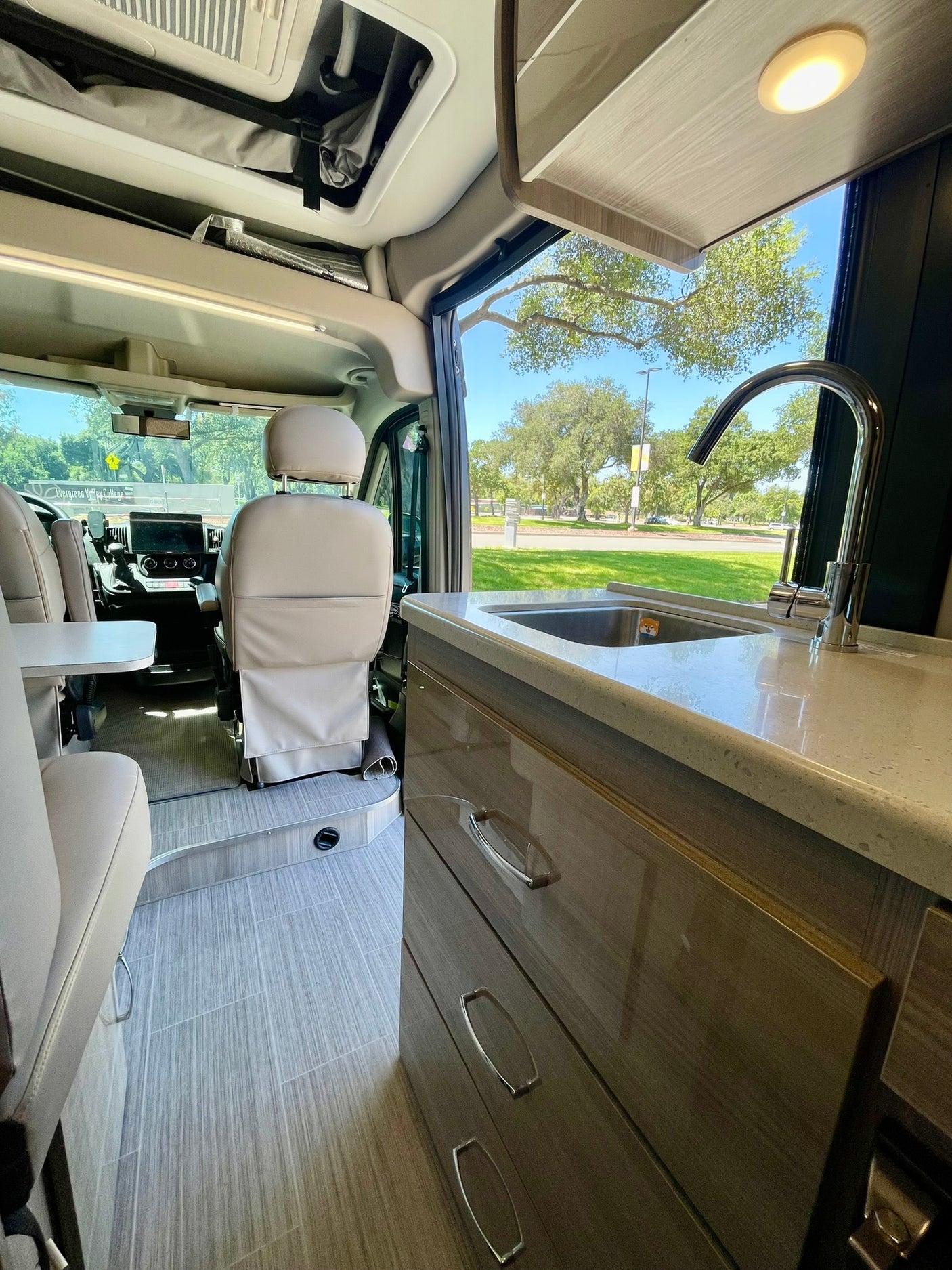Bright rv rental interior showcasing a modern kitchen with sink, comfy front cabin seats, and overhead storage. Enjoy scenic views.