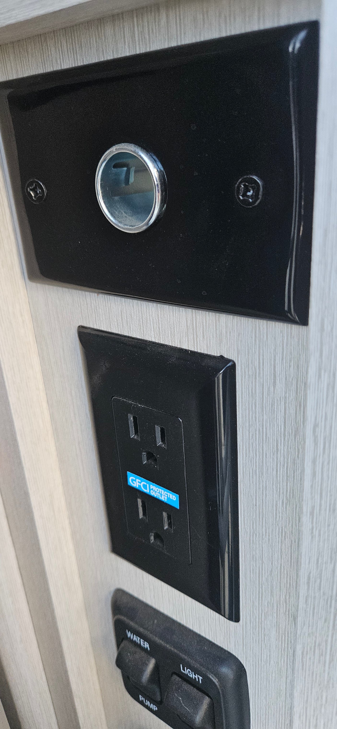RV rental interior: GFCI outlet, water/light/pump controls, and a round metallic component on a black panel.