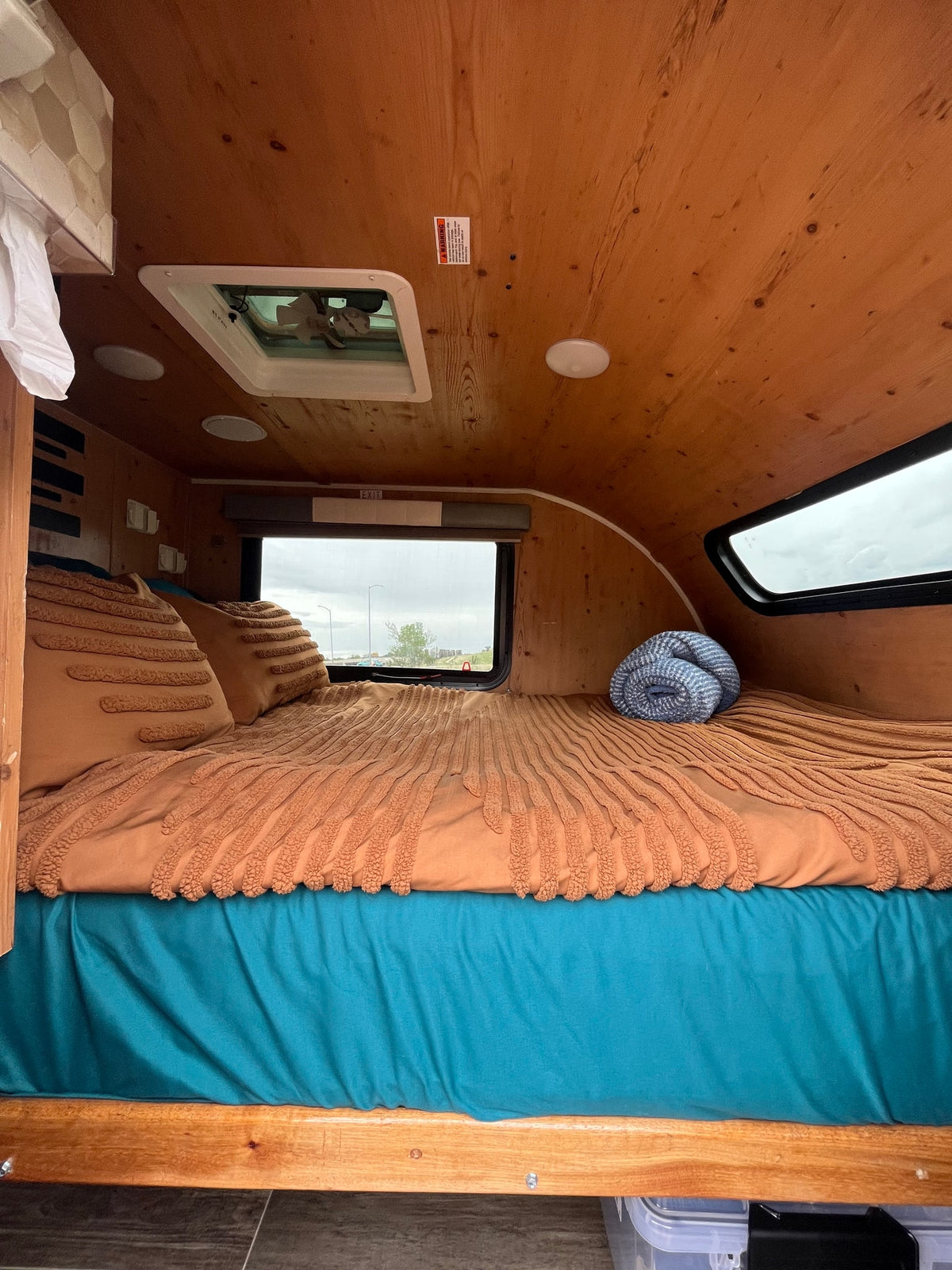 Cozy rv rental interior with warm wood panels. A bed with brown textured bedding, teal sheets, and a blue blanket is set for comfort. — photo 6