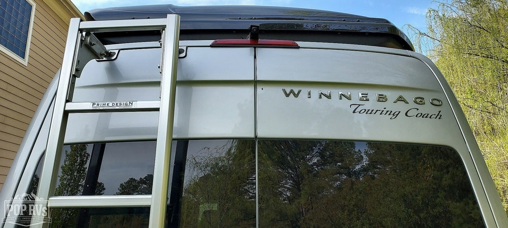 Rear of a silver Winnebago Touring Coach RV rental, featuring a Prime Design ladder and prominent branding.