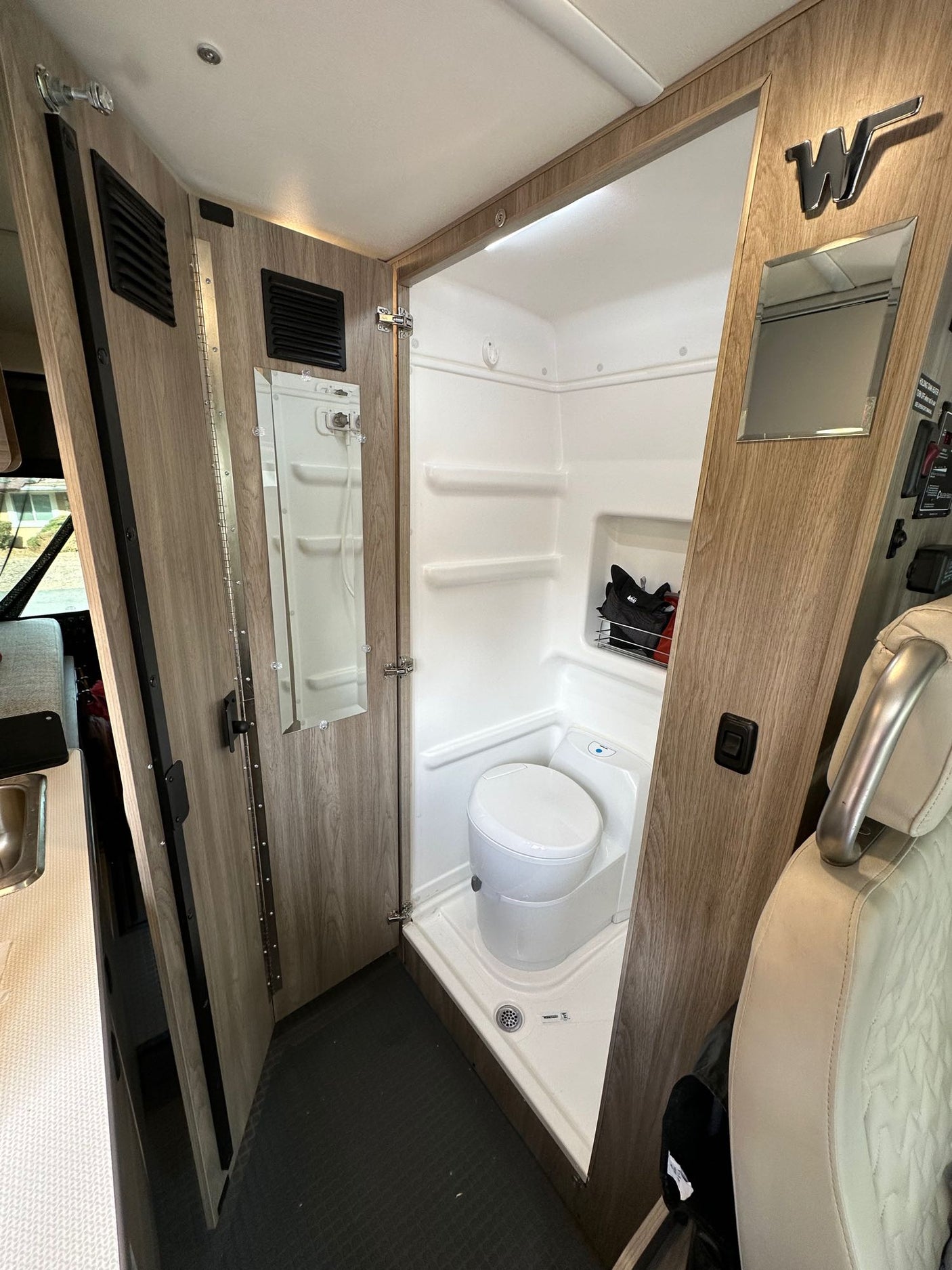 Compact RV rental wet bath interior, featuring a white toilet, shower, and wood-paneled folding door.