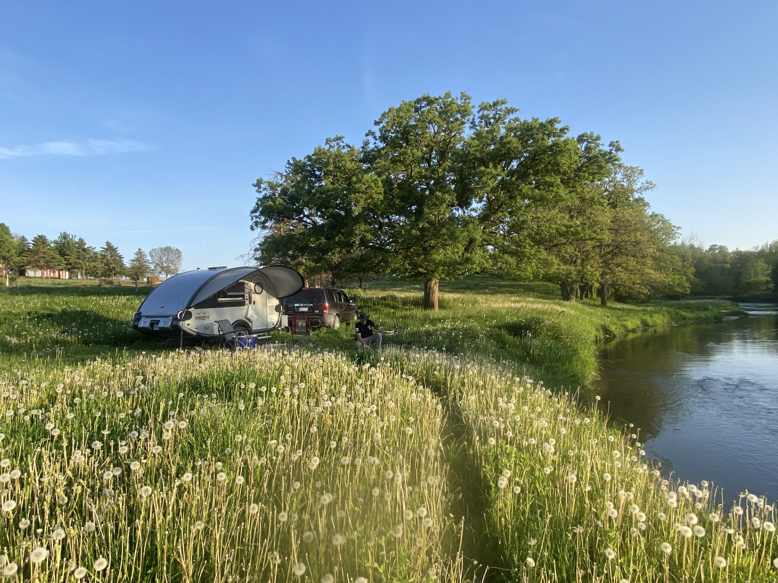 surrounded by dandelions. A person relaxes in nature's calm.|Cozy RV rental adventure: A turquoise #nuCamp mug sits on weathered wood