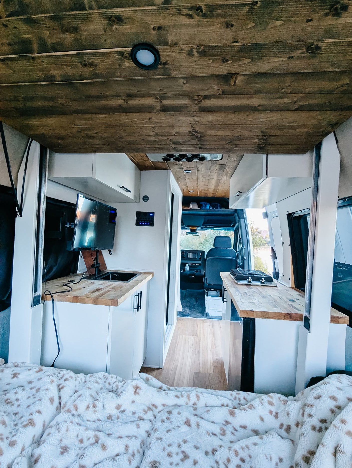 Inside a modern rv rental camper van: rustic wood ceiling, white kitchen with TV, sink, and stove. Cozy blanket in the foreground.