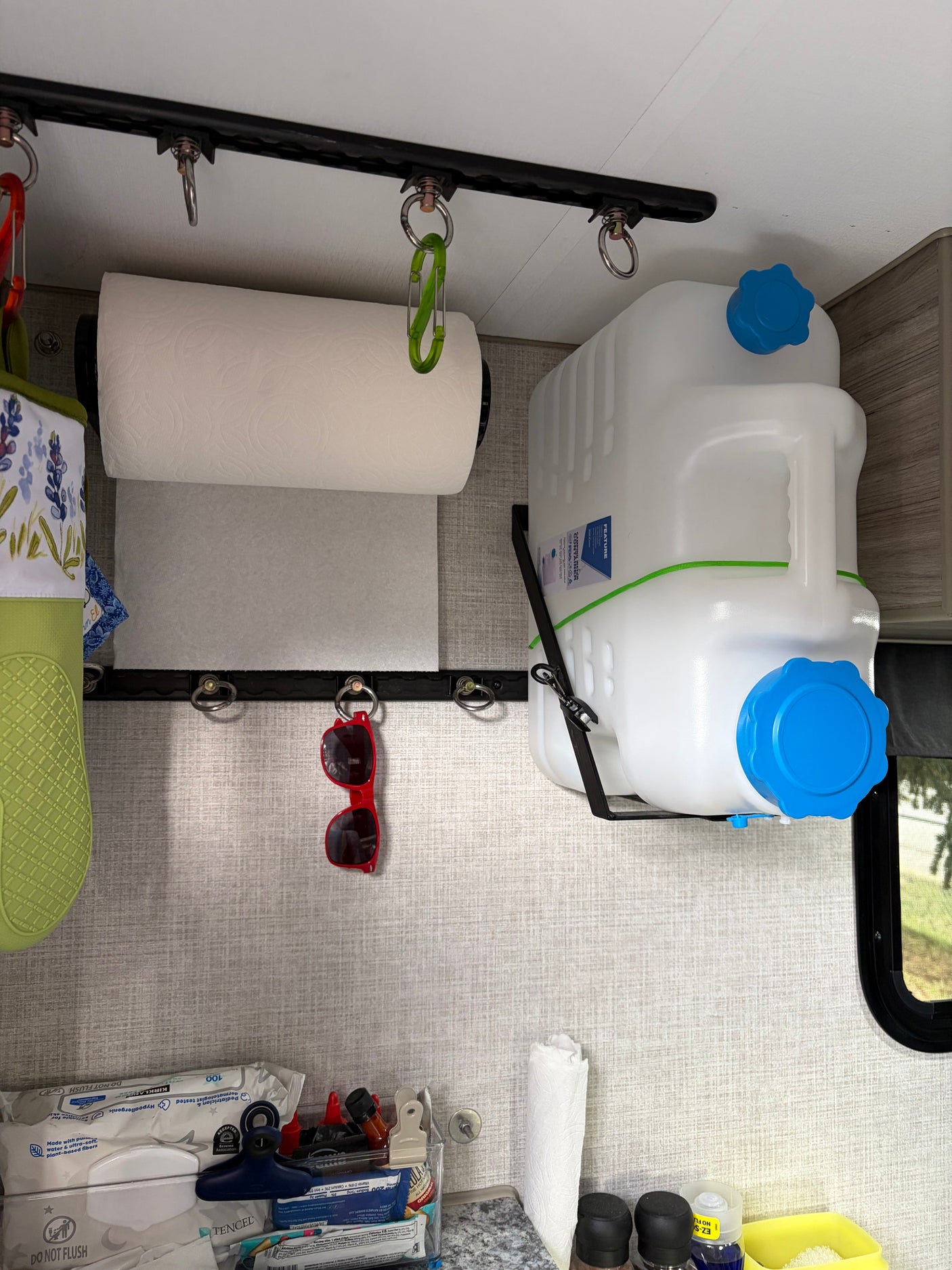 Efficient storage in an RV rental, featuring a paper towel holder, water jug, and utility rails with hooks for small items.