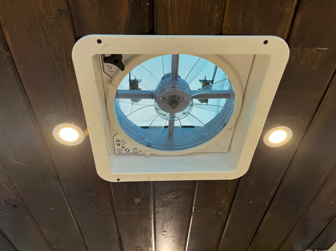 RV rental interior ceiling with a white vent fan, two bright LED lights, and rustic dark wood paneling.