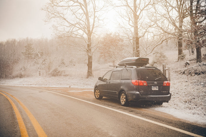 open doors reveal a custom camper setup; two people access the trunk.|Winter journey: A grey minivan with roof cargo box parked on a snowy road. Perfect for a cozy RV rental adventure.|An SUV with a custom camping kitchen: pull-out stove