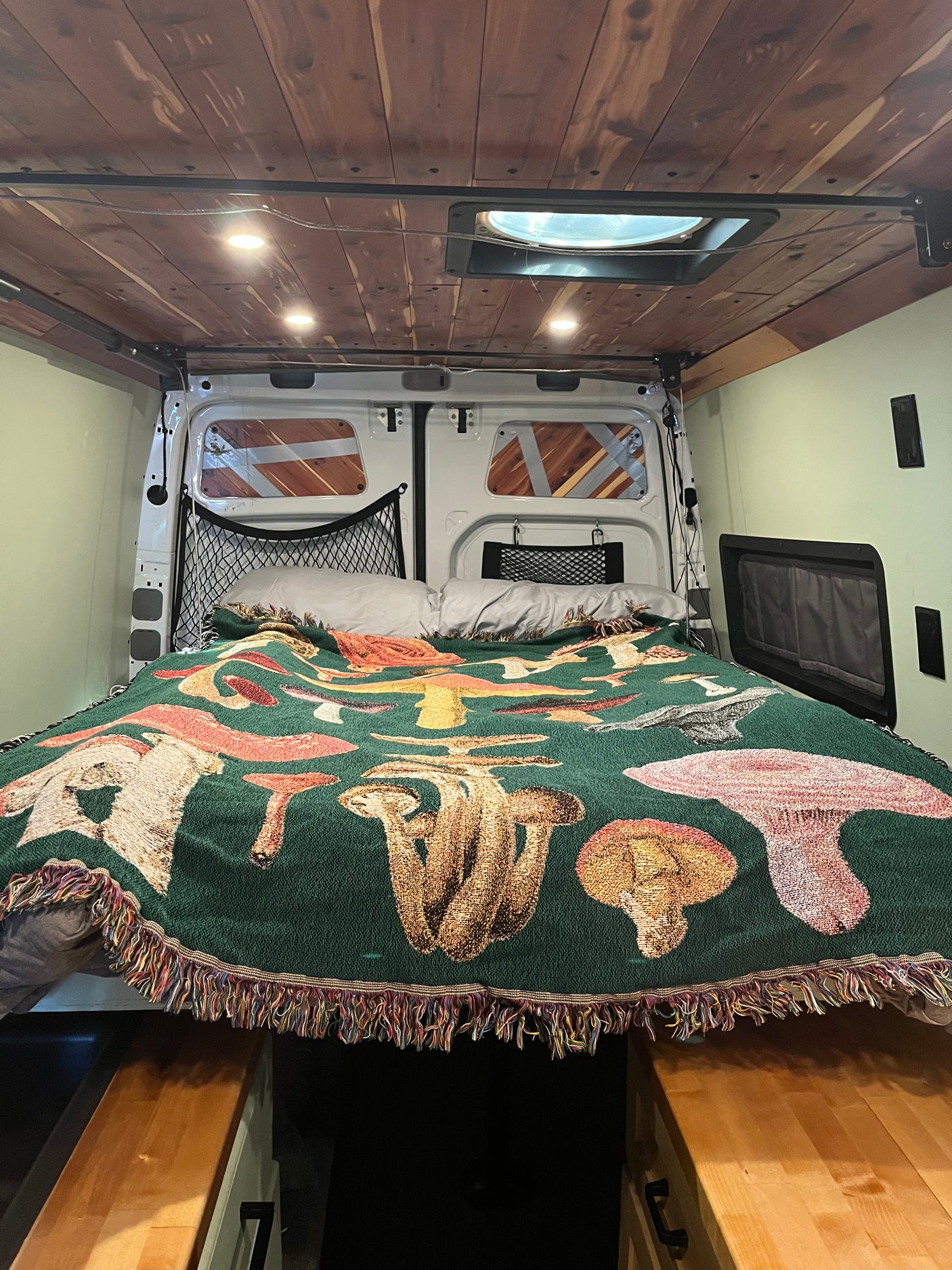 Cozy RV rental bedroom with a mushroom blanket, wooden ceiling, and skylight in a van conversion.