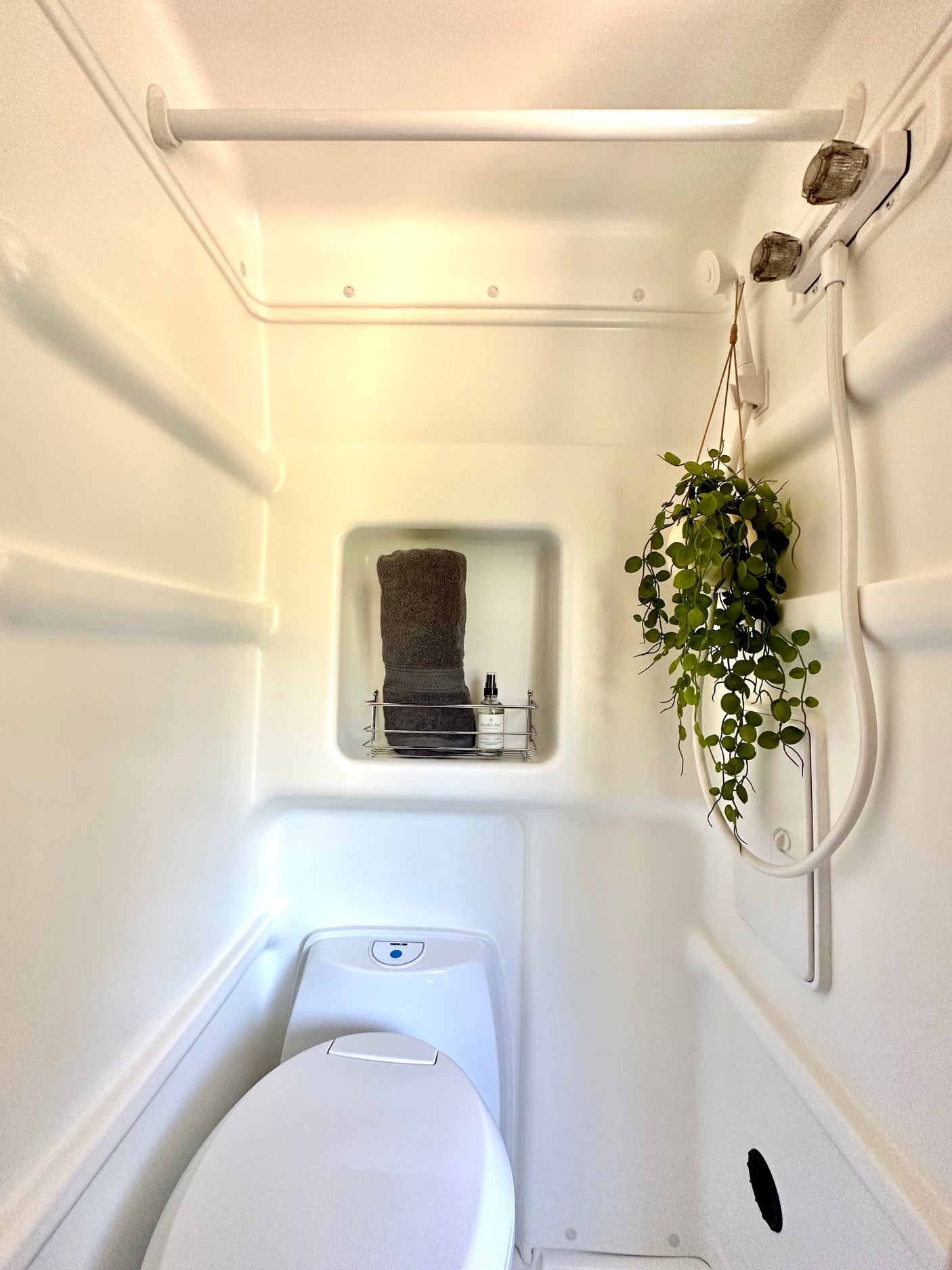 This clean RV rental bathroom features a compact toilet, handheld shower, and recessed shelf for essentials.