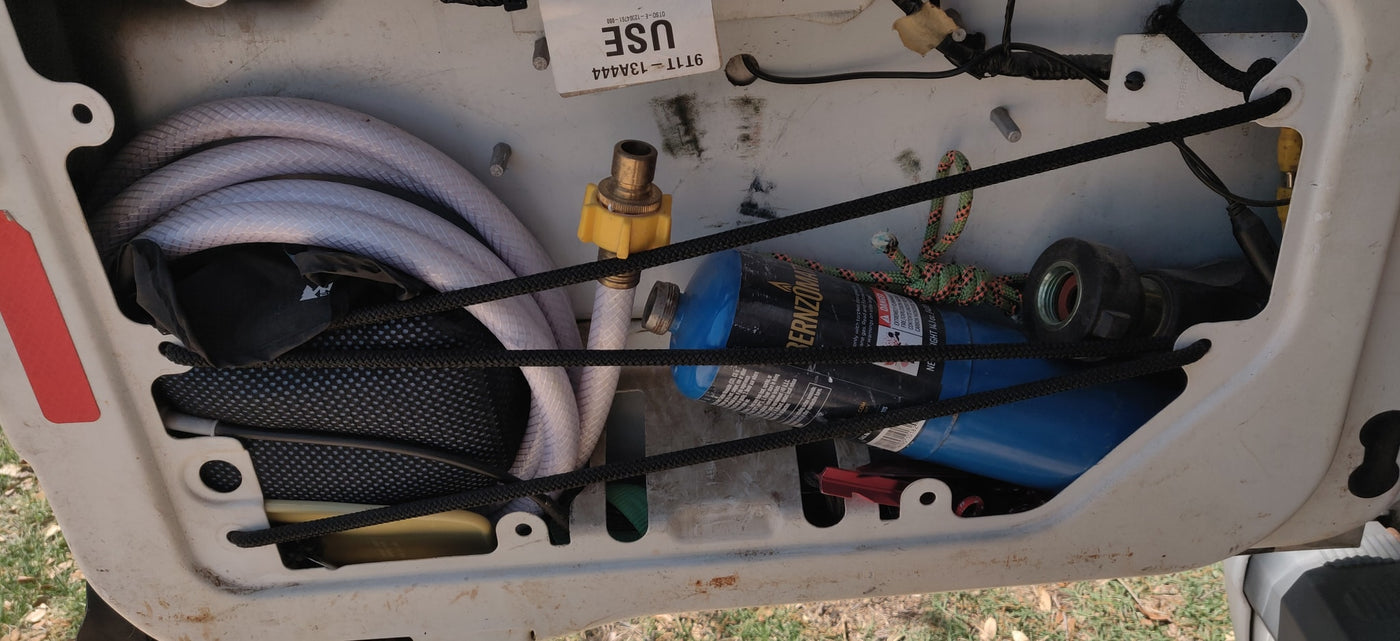 An RV rental storage compartment holds coiled white hoses, blue propane tanks, and brass fittings, secured by elastic cords. — photo 7