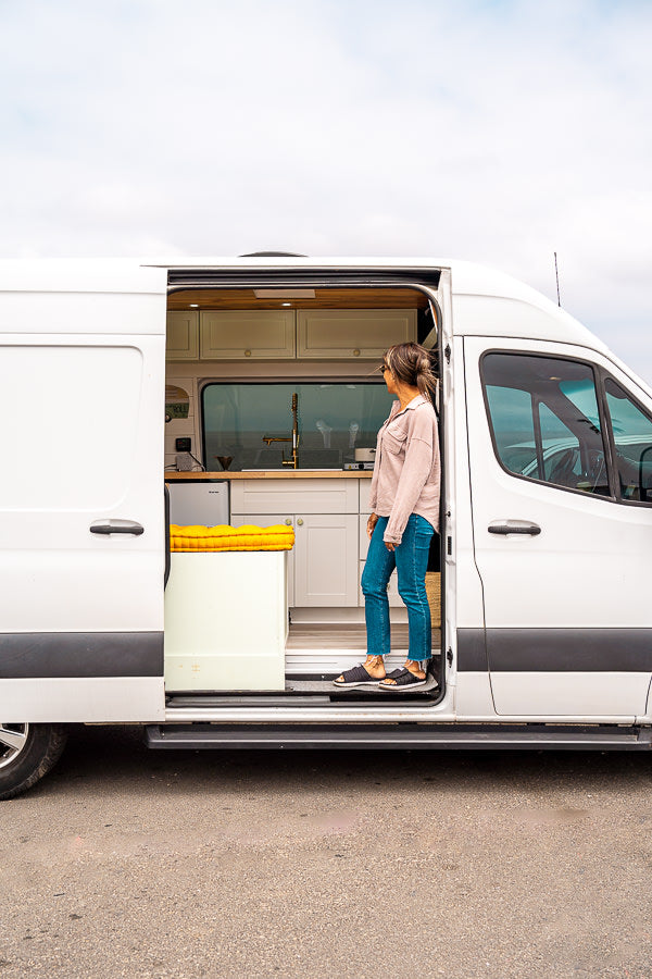 Step into adventure! A woman explores a modern RV rental's inviting, fully-equipped van kitchen.