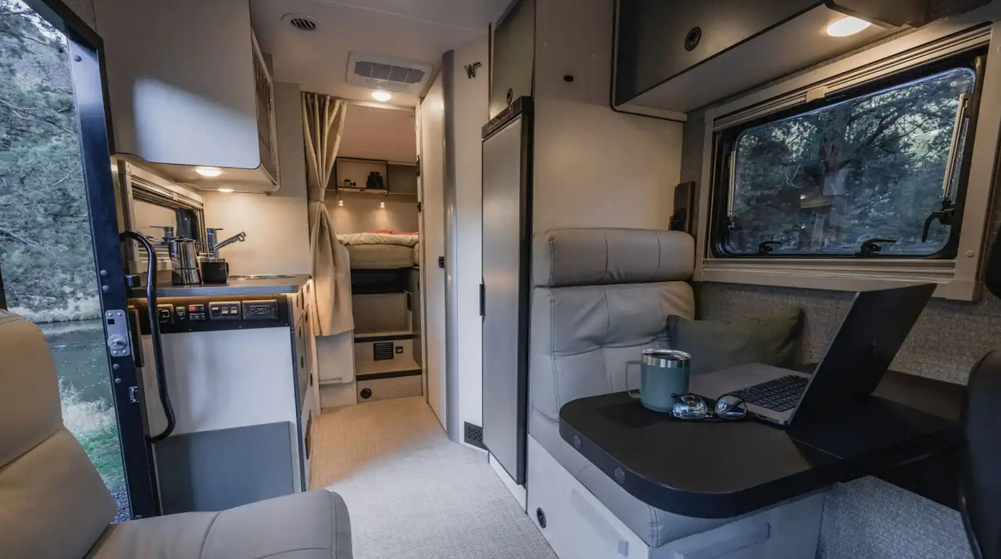 Step inside this modern rv rental, revealing a functional kitchen, comfortable lounge with laptop, and rear bunk beds.