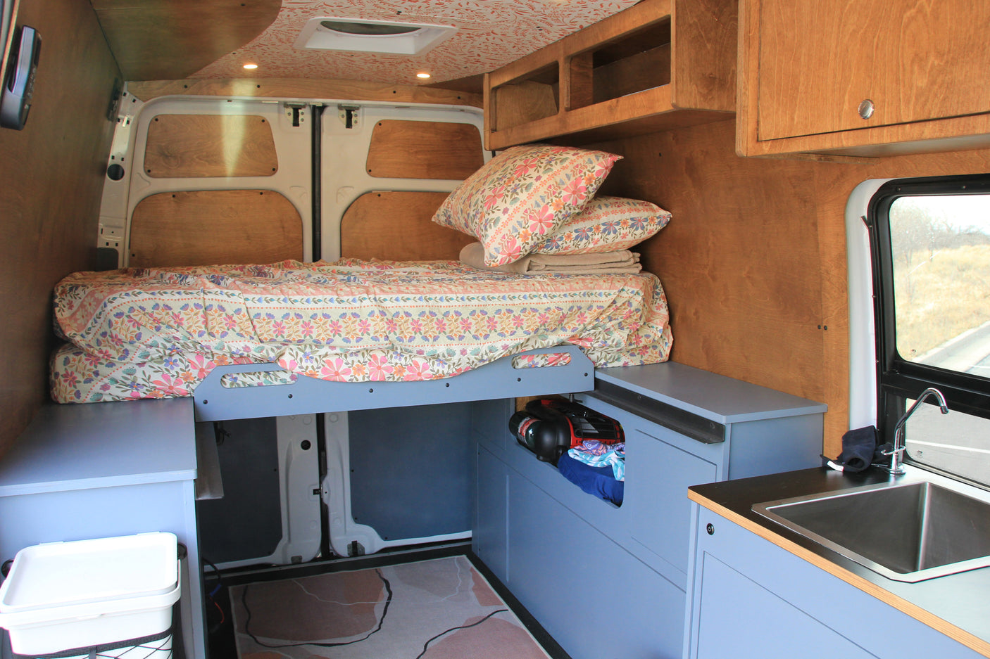 This rv rental features a well-designed camper van interior with a comfy bed, kitchen sink, and ample storage.