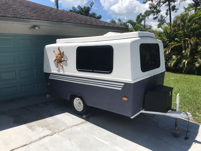 featuring a blue and white RV rental parked at a serene campsite with hookups.|A small white and dark gray travel trailer