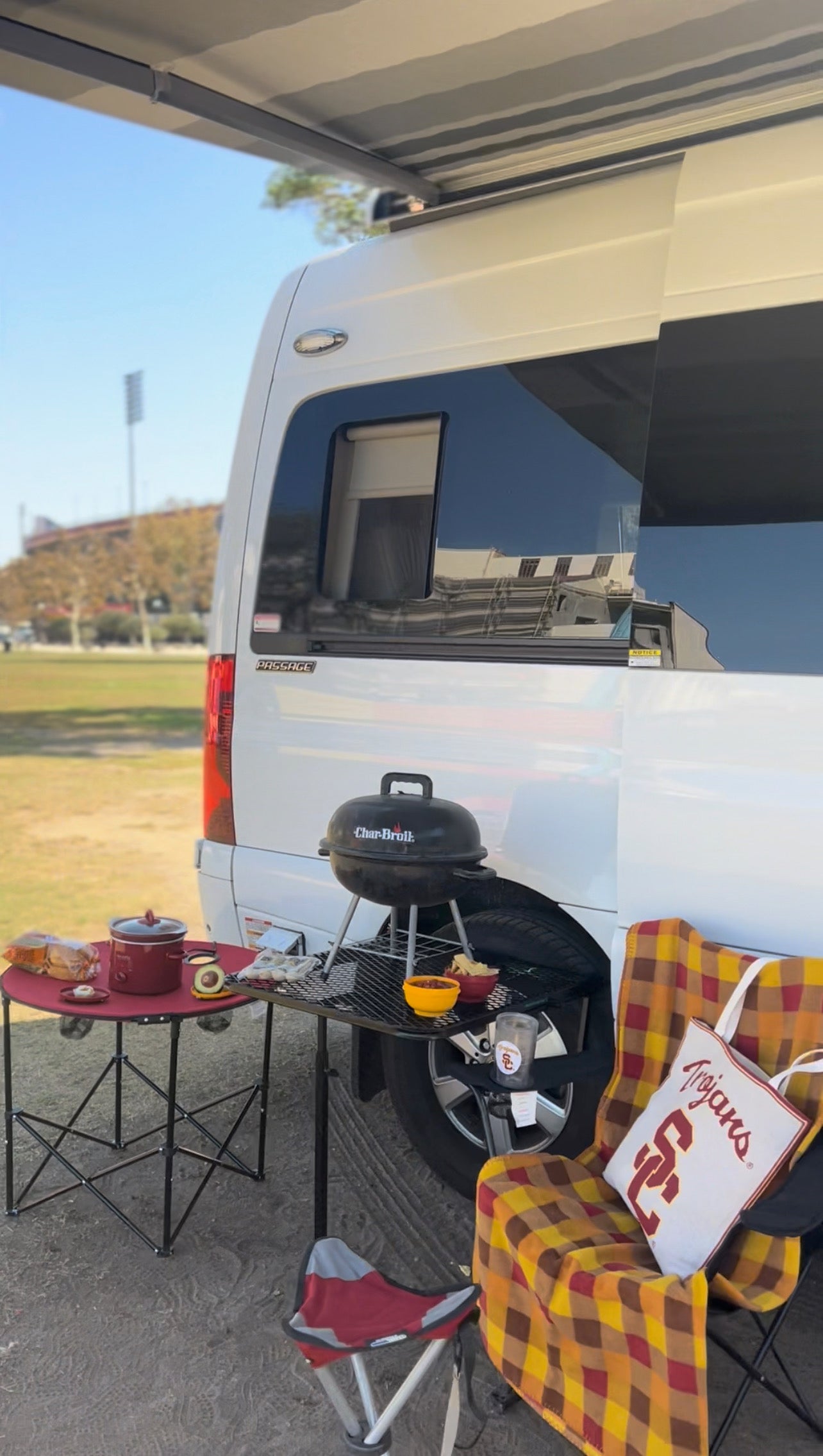 An RV rental provides a perfect tailgate setup: a white camper van with awning, grill, food, & chairs for USC game day.