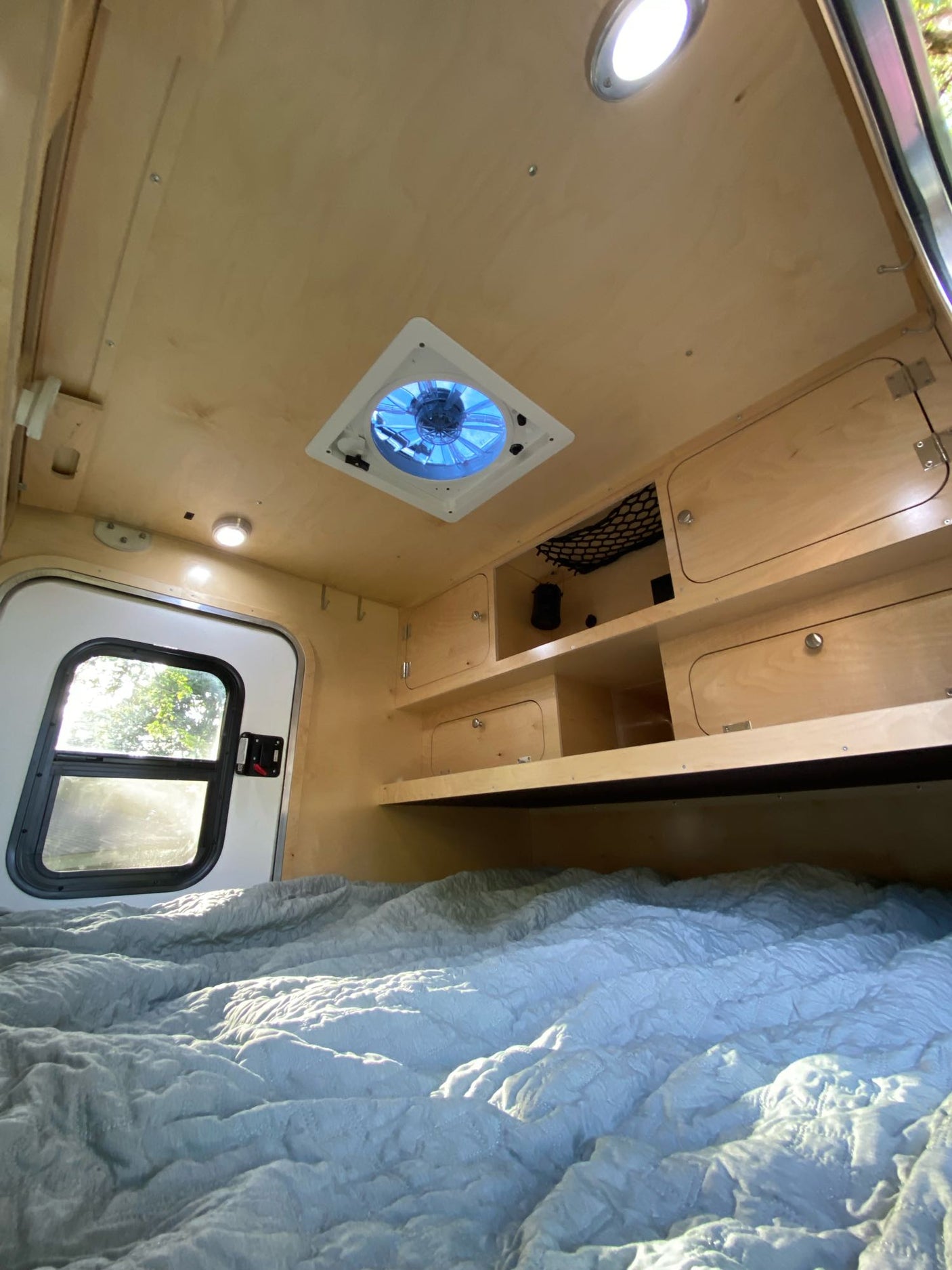Cozy RV rental interior with a comfy bed, large window, ceiling fan, and built-in wooden storage. Perfect for compact travel.