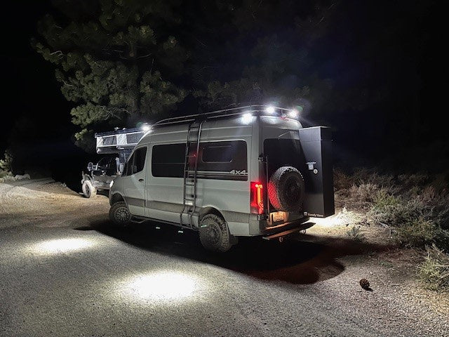 Illuminated 4x4 camper van & SUV parked on a dirt road at night, showcasing an RV rental for rugged outdoor adventures.