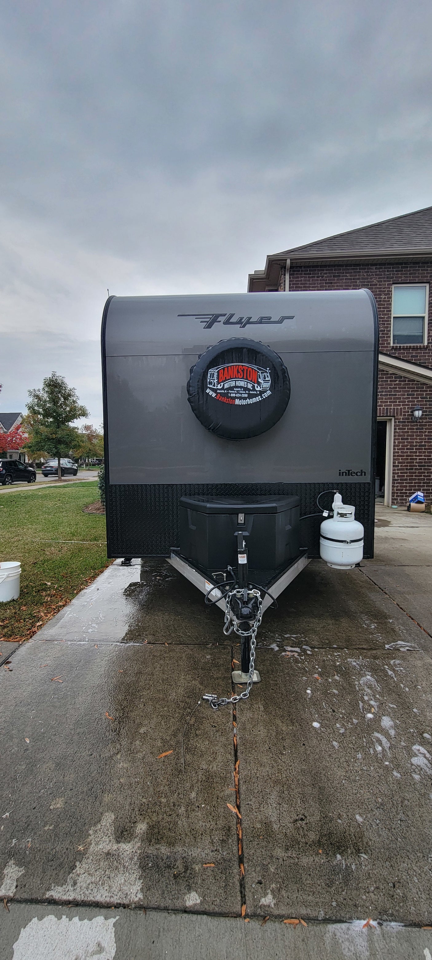 Front of a gray InTech Flyer travel trailer, likely an rv rental from Bankston Motor Homes, on a wet driveway.