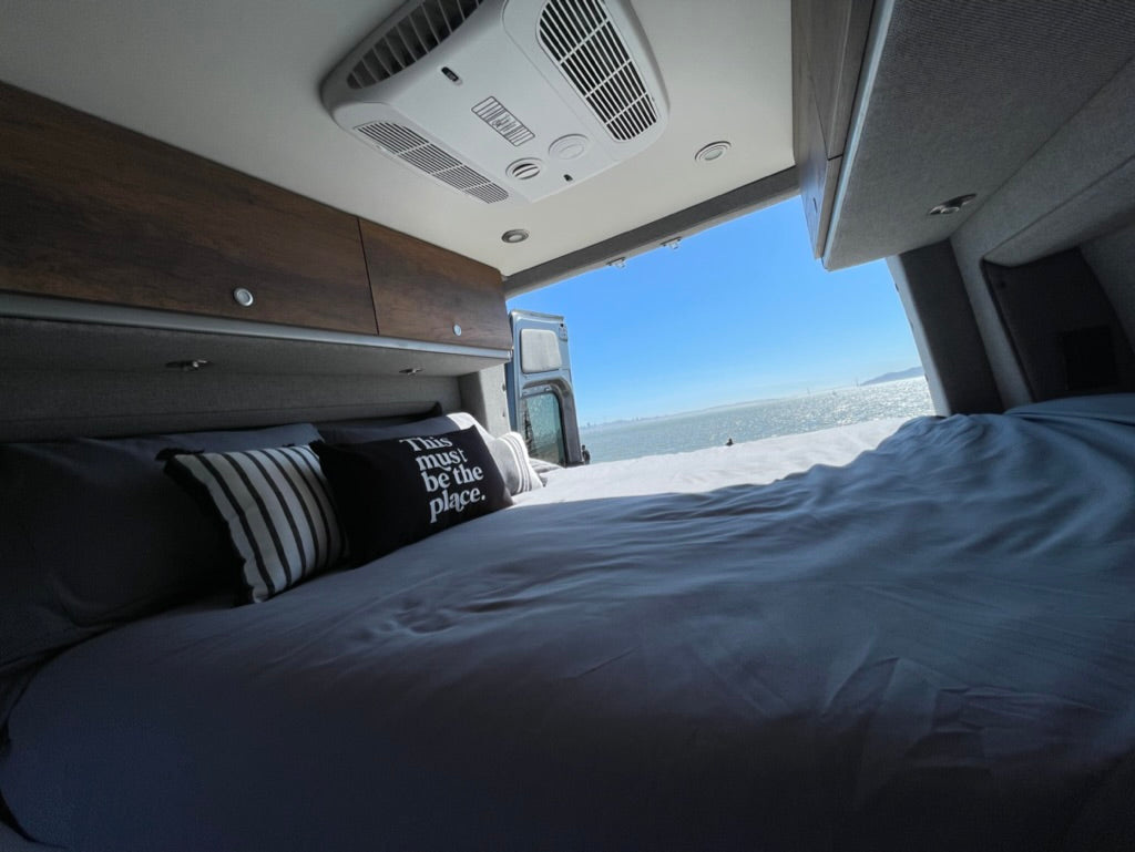 Cozy RV rental interior with a comfy bed offering breathtaking bay views from the open rear doors, perfect for relaxing travel.
