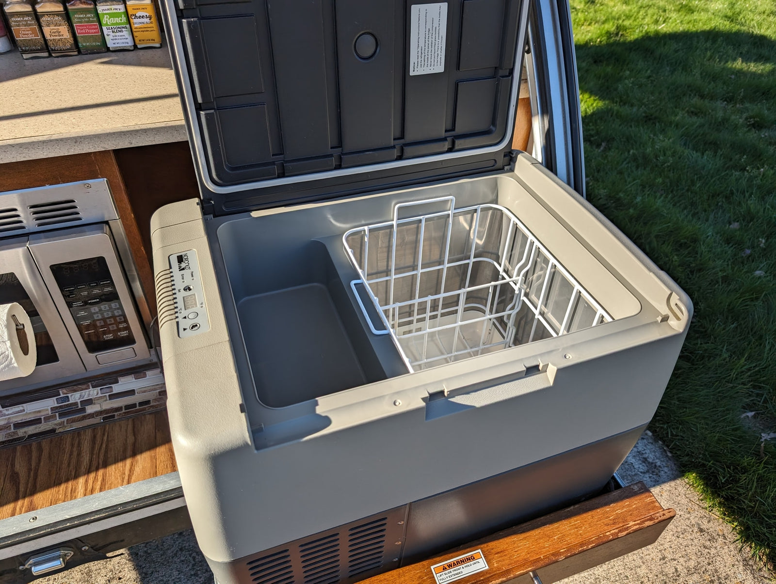 open window showing blue sky & car.|RV rental interior with open wooden cabinets showing shelves