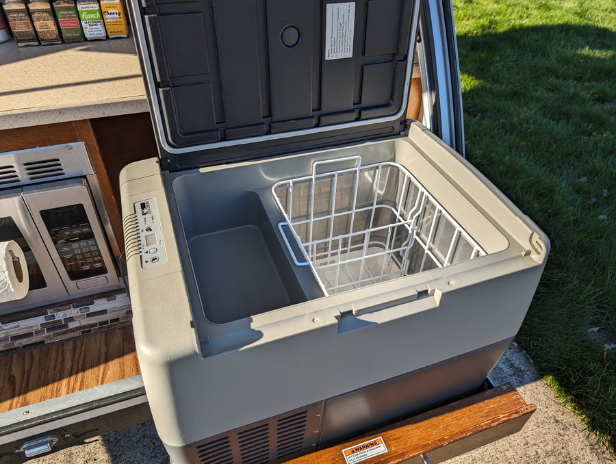 open window showing blue sky & car.|RV rental interior with open wooden cabinets showing shelves