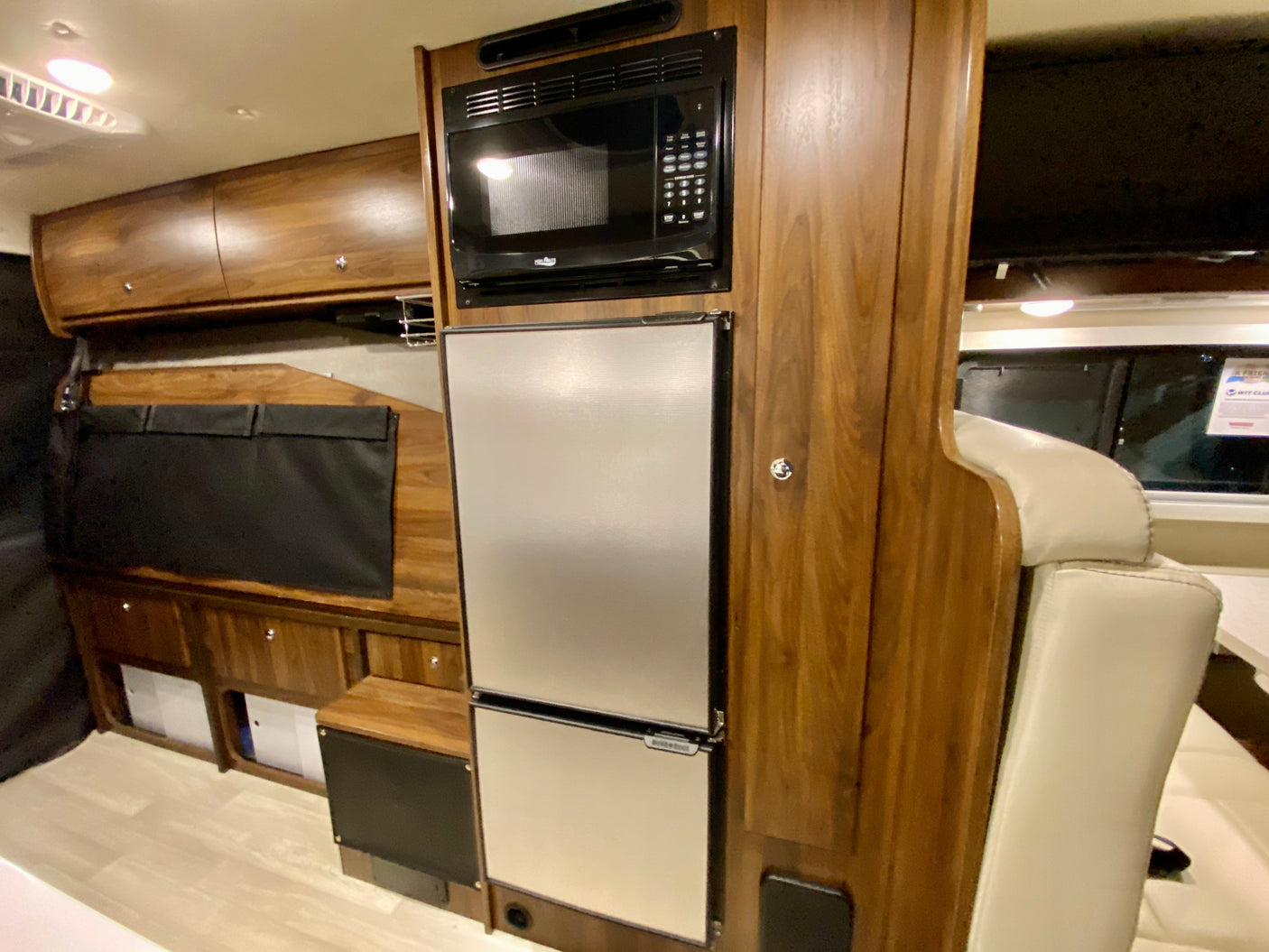 This RV rental interior offers a compact kitchen with a microwave, refrigerator, and wooden cabinetry, plus a covered TV and seating.