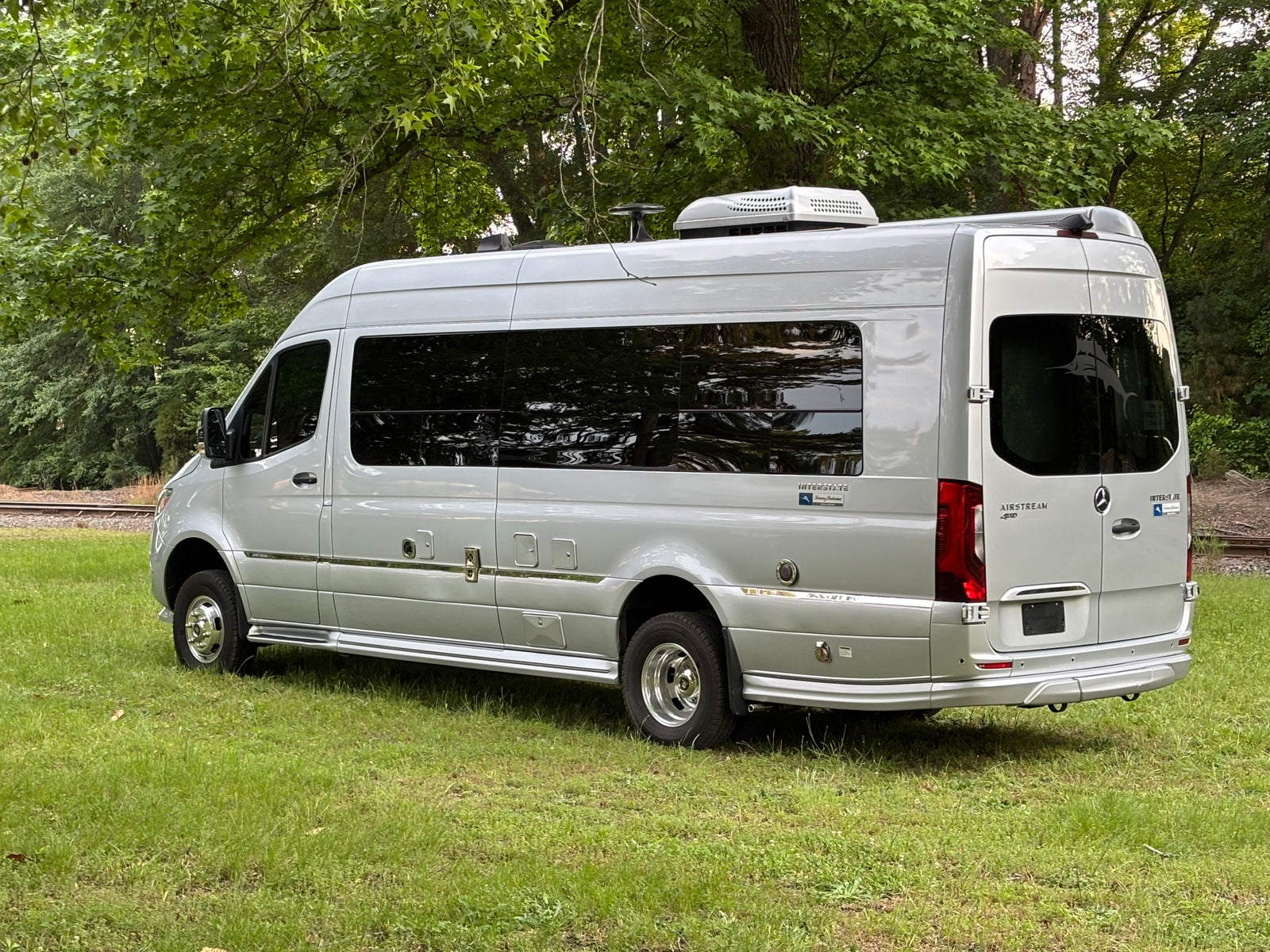Silver Airstream Interstate touring coach RV parked on grass near tracks, great for rv rental.