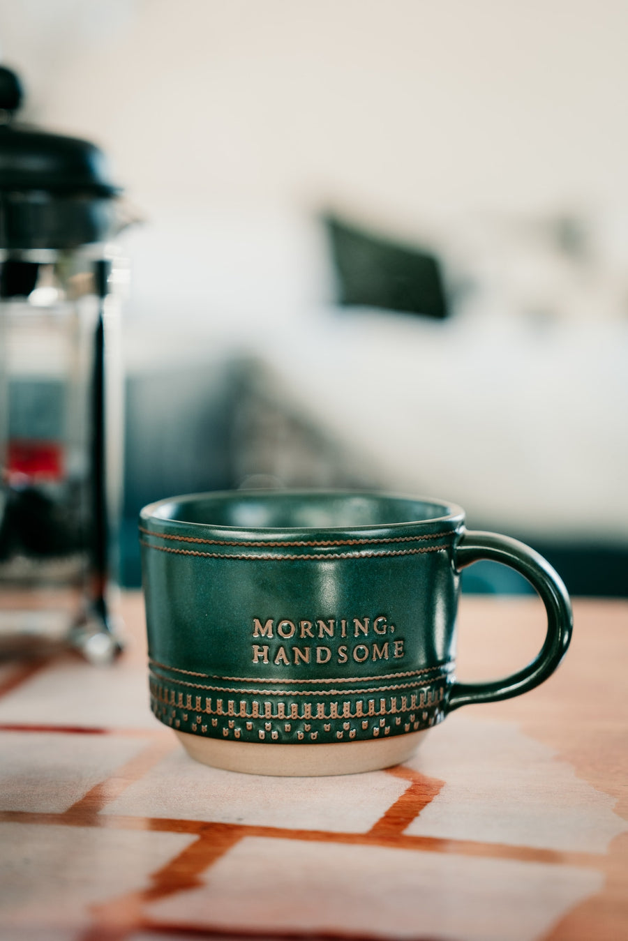 Cozy morning in an RV rental: green 'MORNING, HANDSOME' mug & French press coffee maker.
