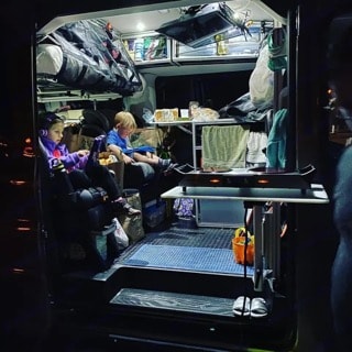 Cozy camper interior! Two kids relax inside their bright **RV rental**, featuring compact kitchen & storage for family van life camping.