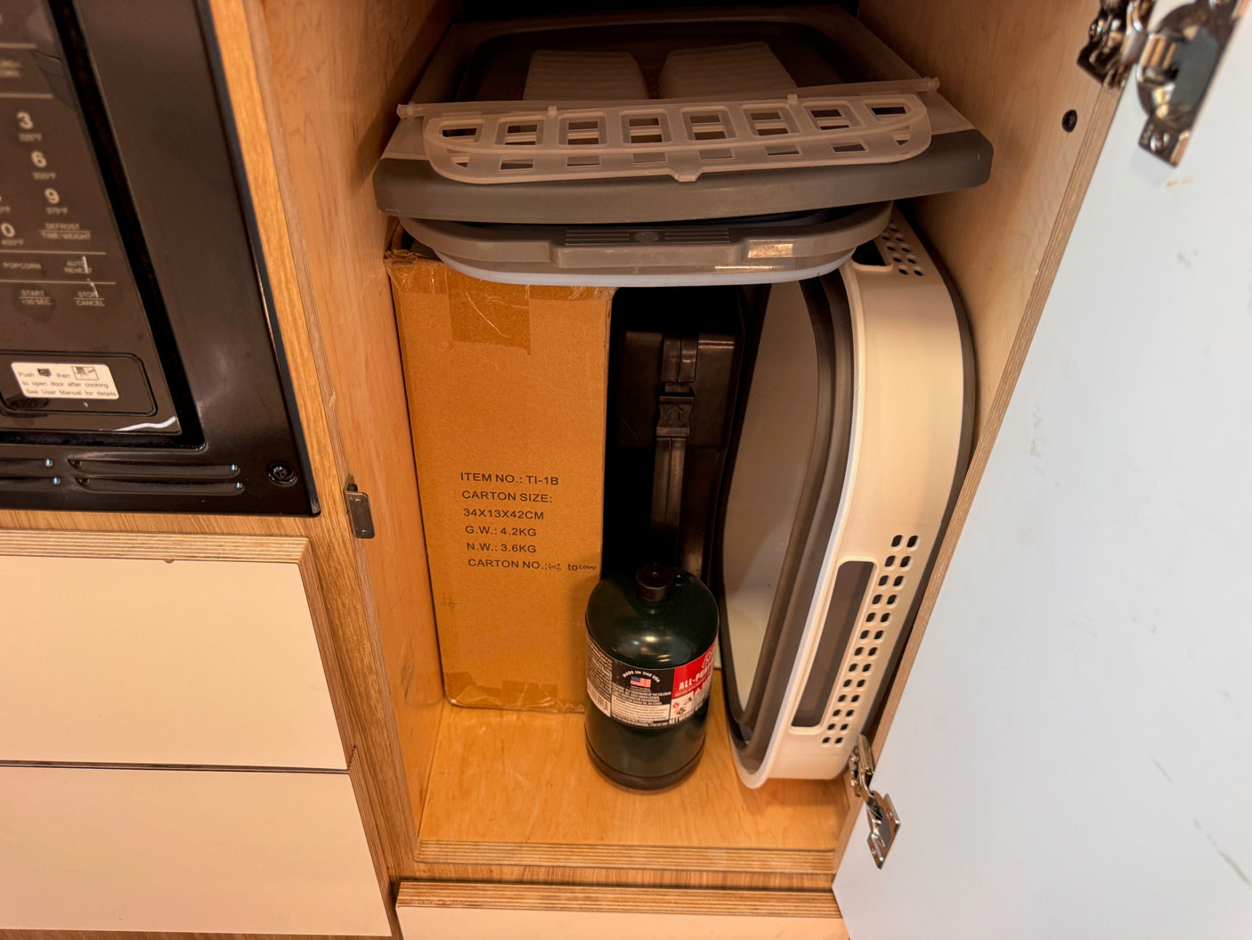 RV rental kitchen cabinet reveals compact storage: collapsible items, a propane tank, and a microwave.
