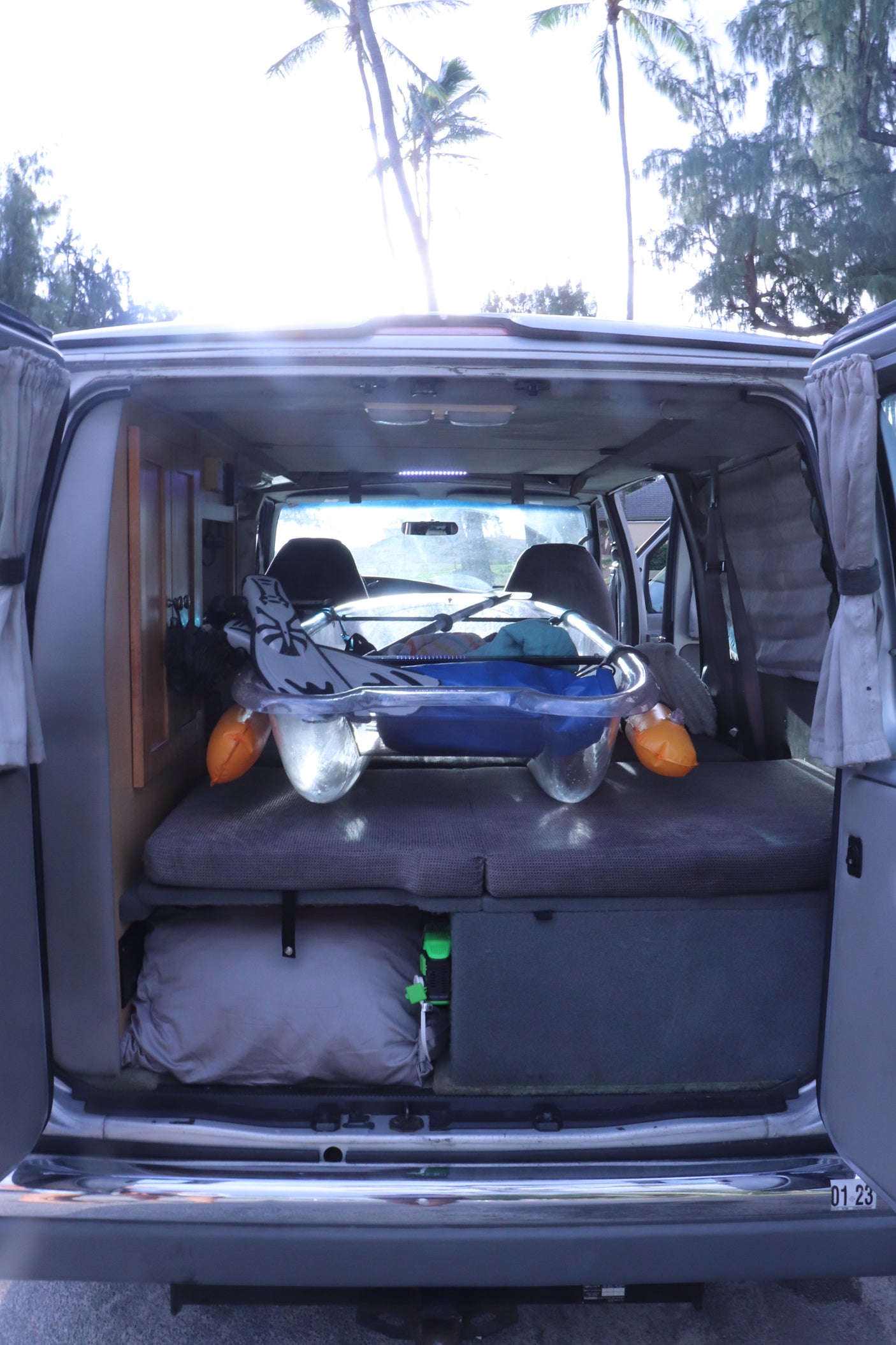 RV rental interior featuring organized gear storage, a convertible bed, and a sunny view of palm trees, ideal for travel adventures.