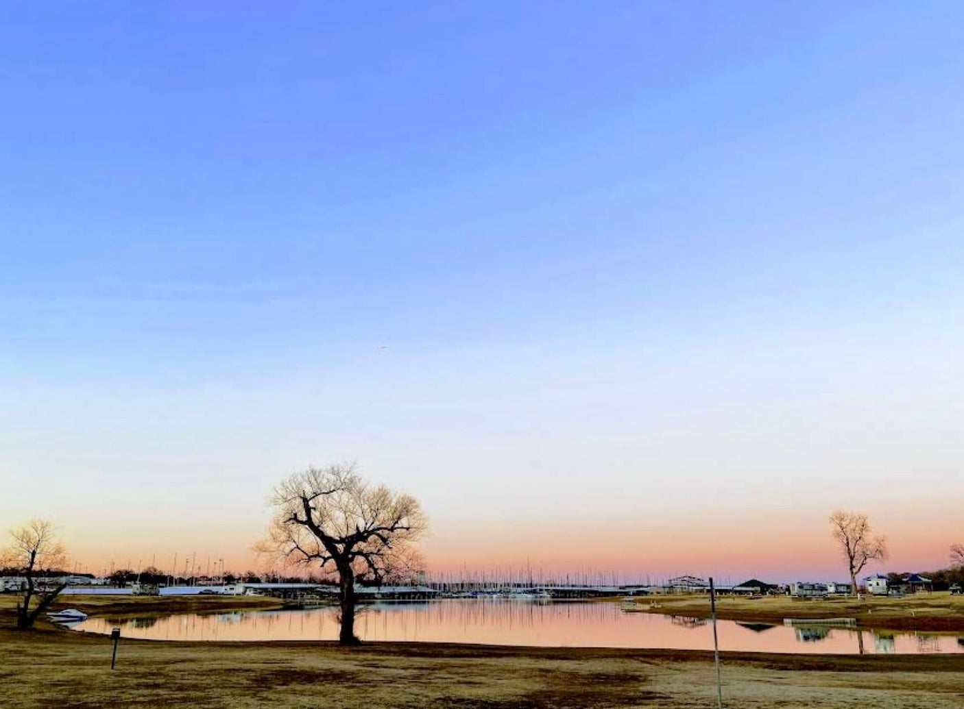 Tranquil sunset over a marina with bare trees & still water. RVs are seen near the shore, perfect for an RV rental vacation.