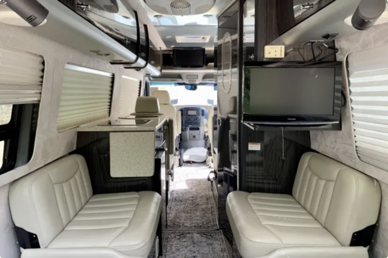 Spacious RV rental interior featuring comfortable seating, a compact kitchen, and TV for enjoyable travels.