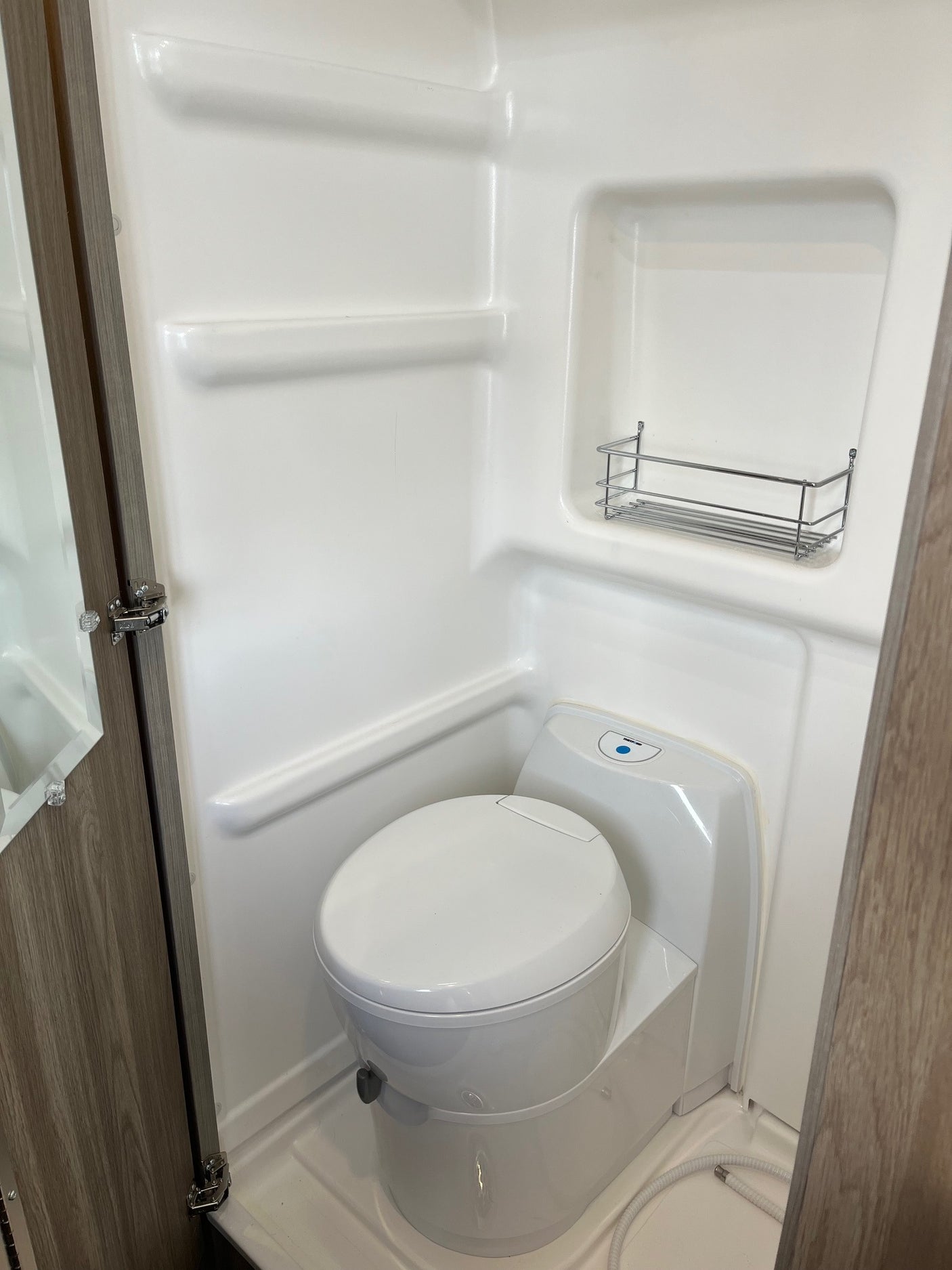 Inside an RV rental's compact wet bath, featuring a toilet, built-in shelving, and a shower hose for convenience.