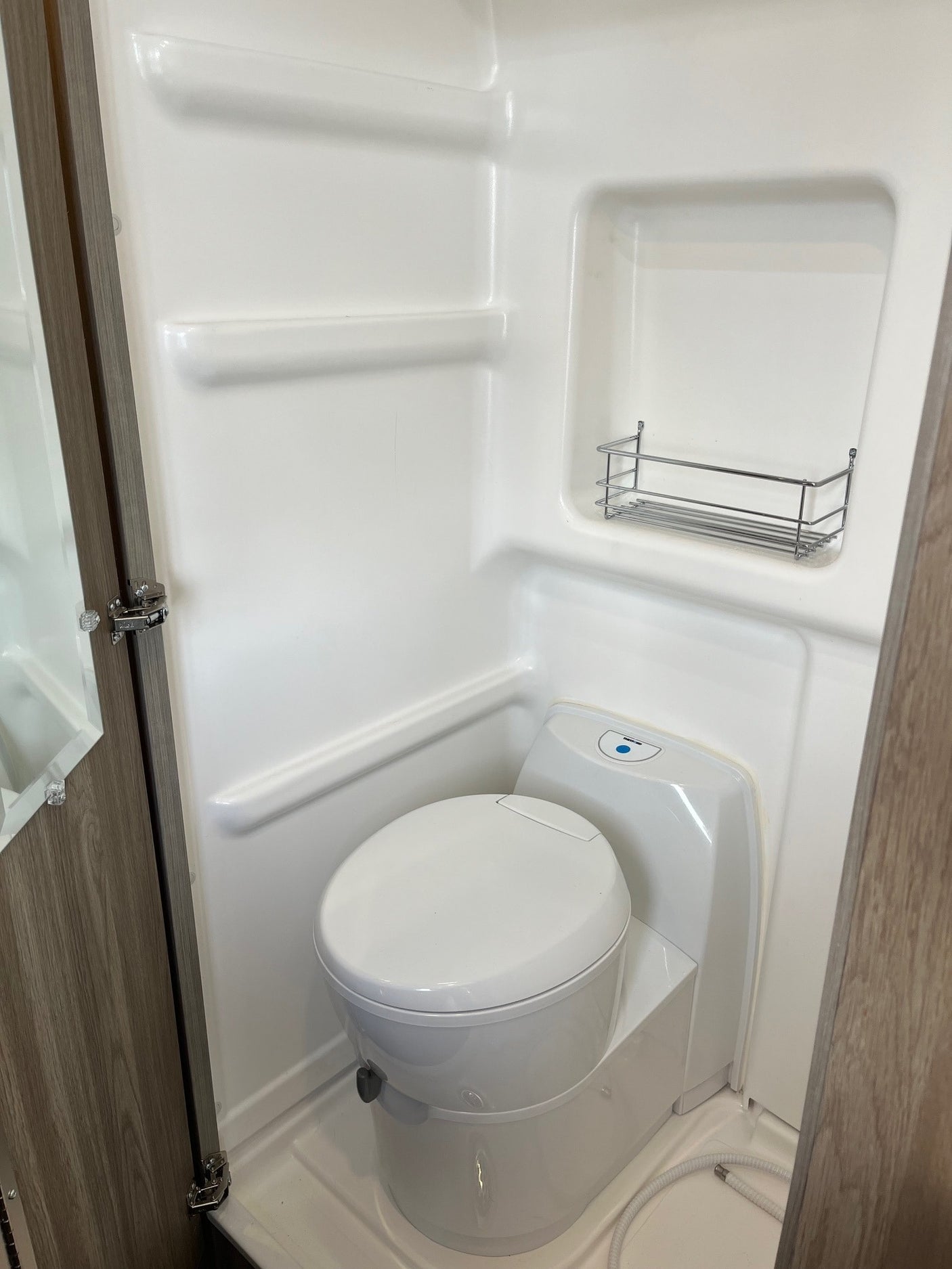 Inside an RV rental's compact wet bath, featuring a toilet, built-in shelving, and a shower hose for convenience.