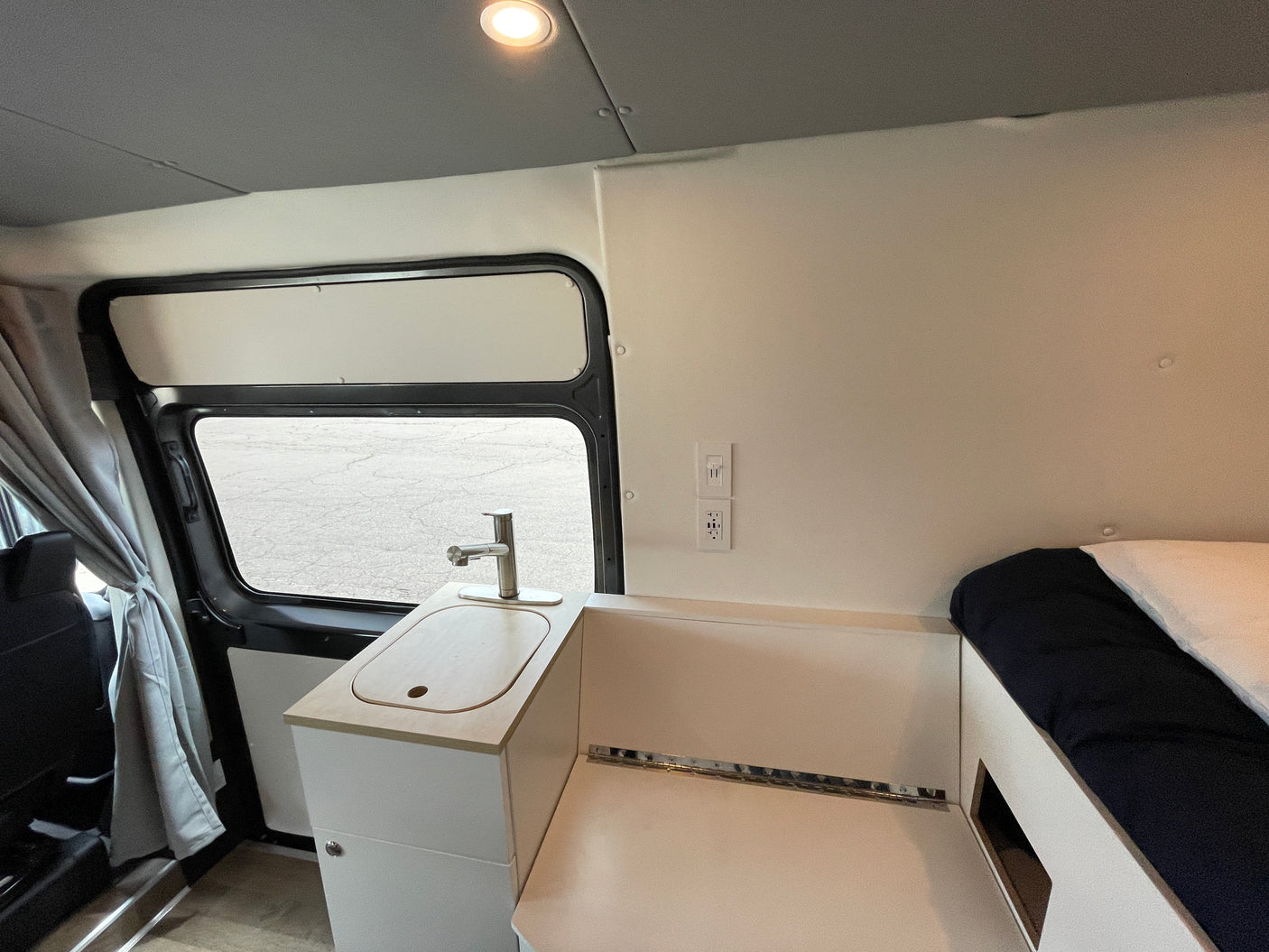 Interior of an RV rental featuring a compact kitchen with a sink, faucet, power outlets, and adjacent sleeping area.