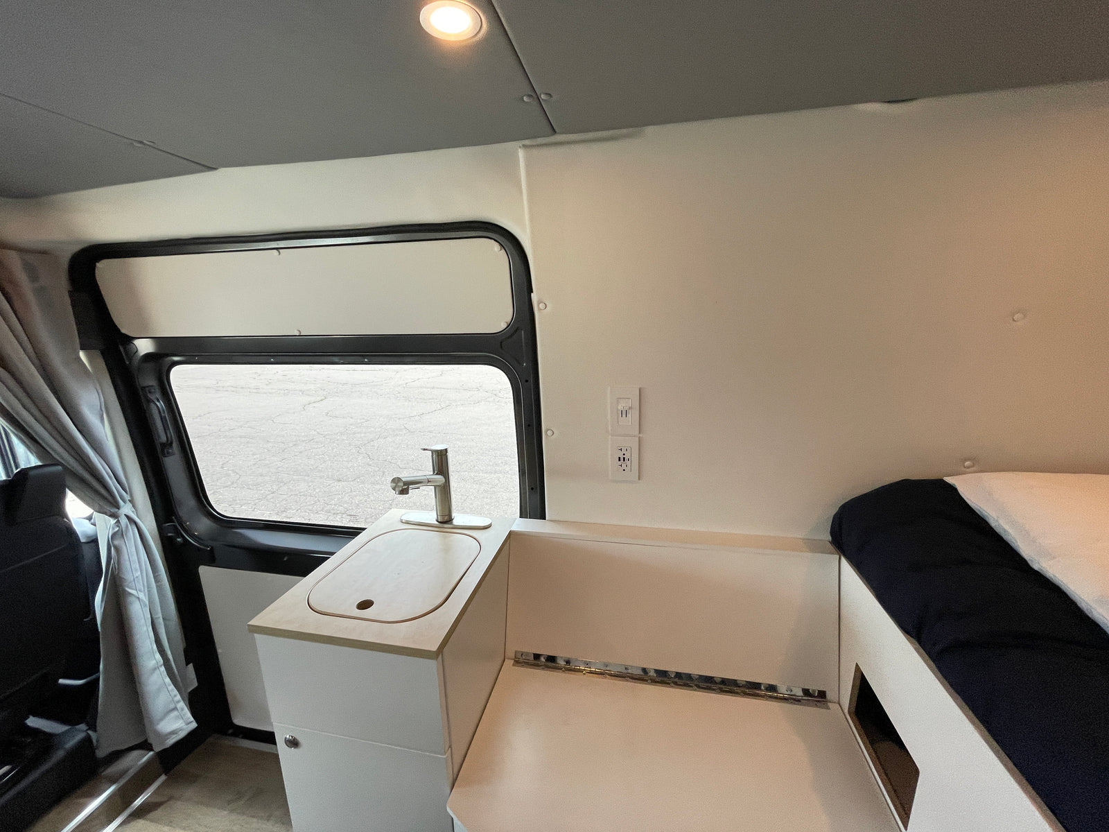 Interior of an RV rental featuring a compact kitchen with a sink, faucet, power outlets, and adjacent sleeping area.