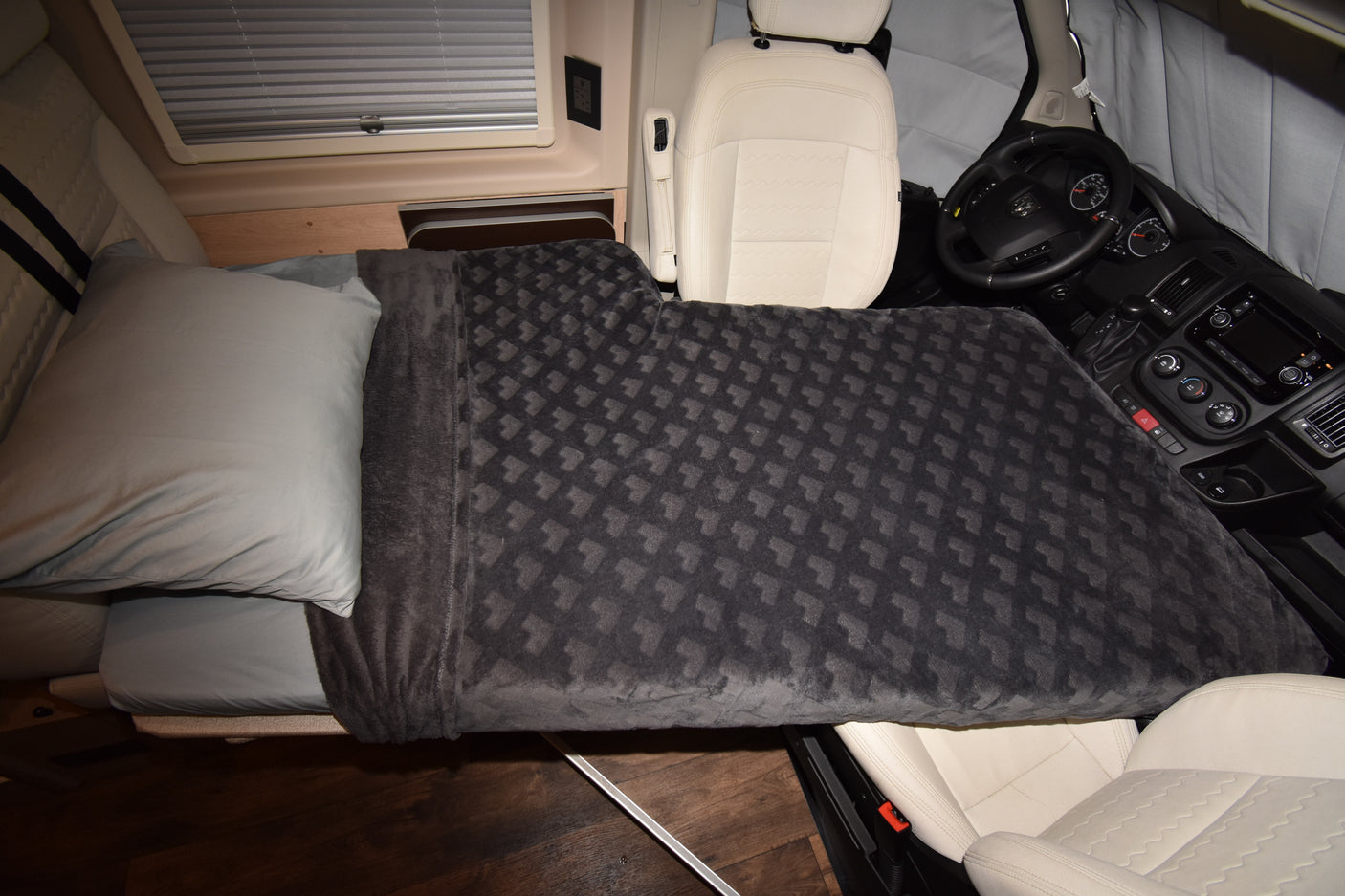 Cozy bed in an RV rental, featuring a grey pillow and patterned blanket extending towards the driver's seat and dashboard.