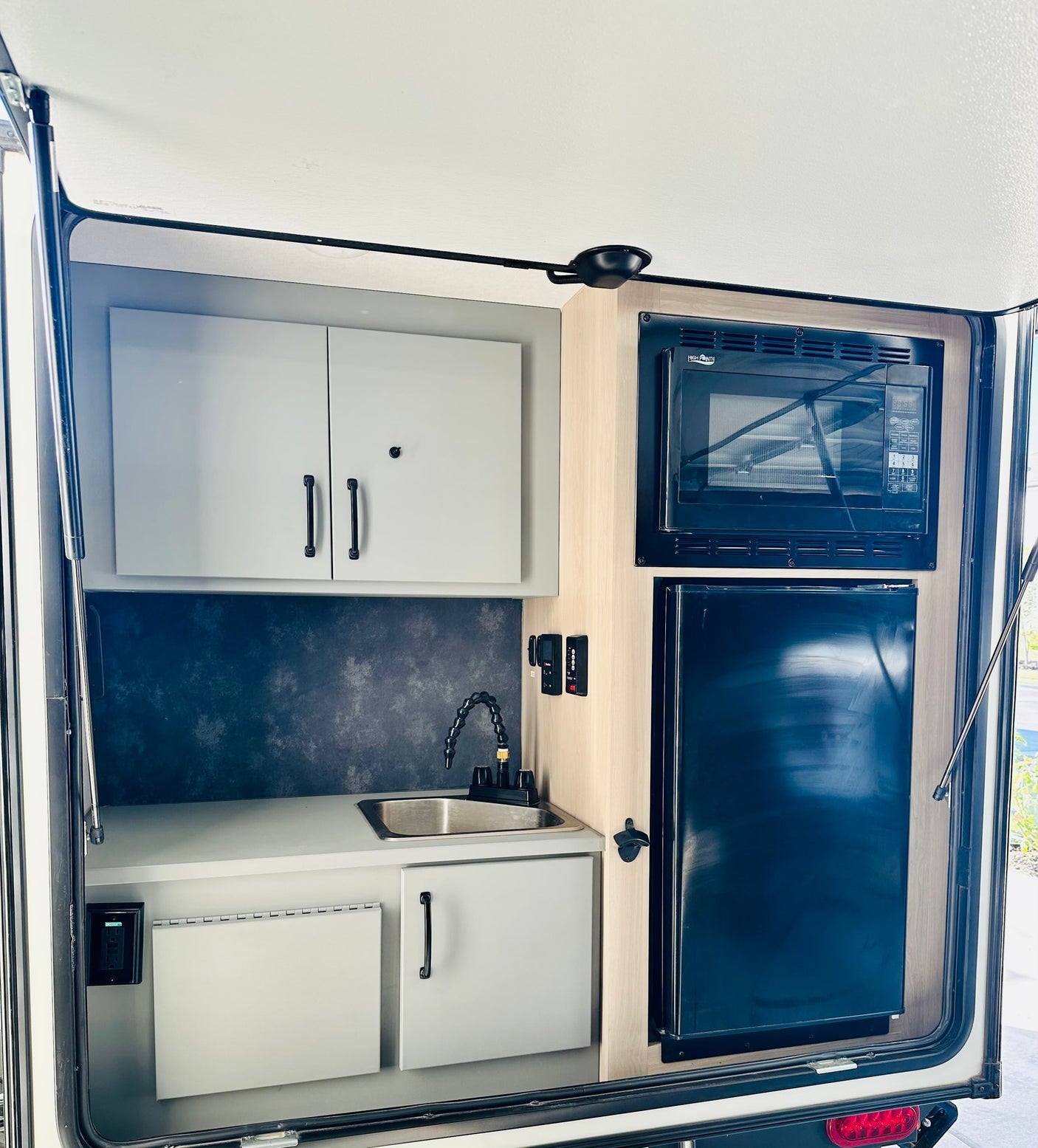 Interior of an rv rental kitchen, featuring a black microwave, refrigerator, stainless steel sink, and white storage cabinets.