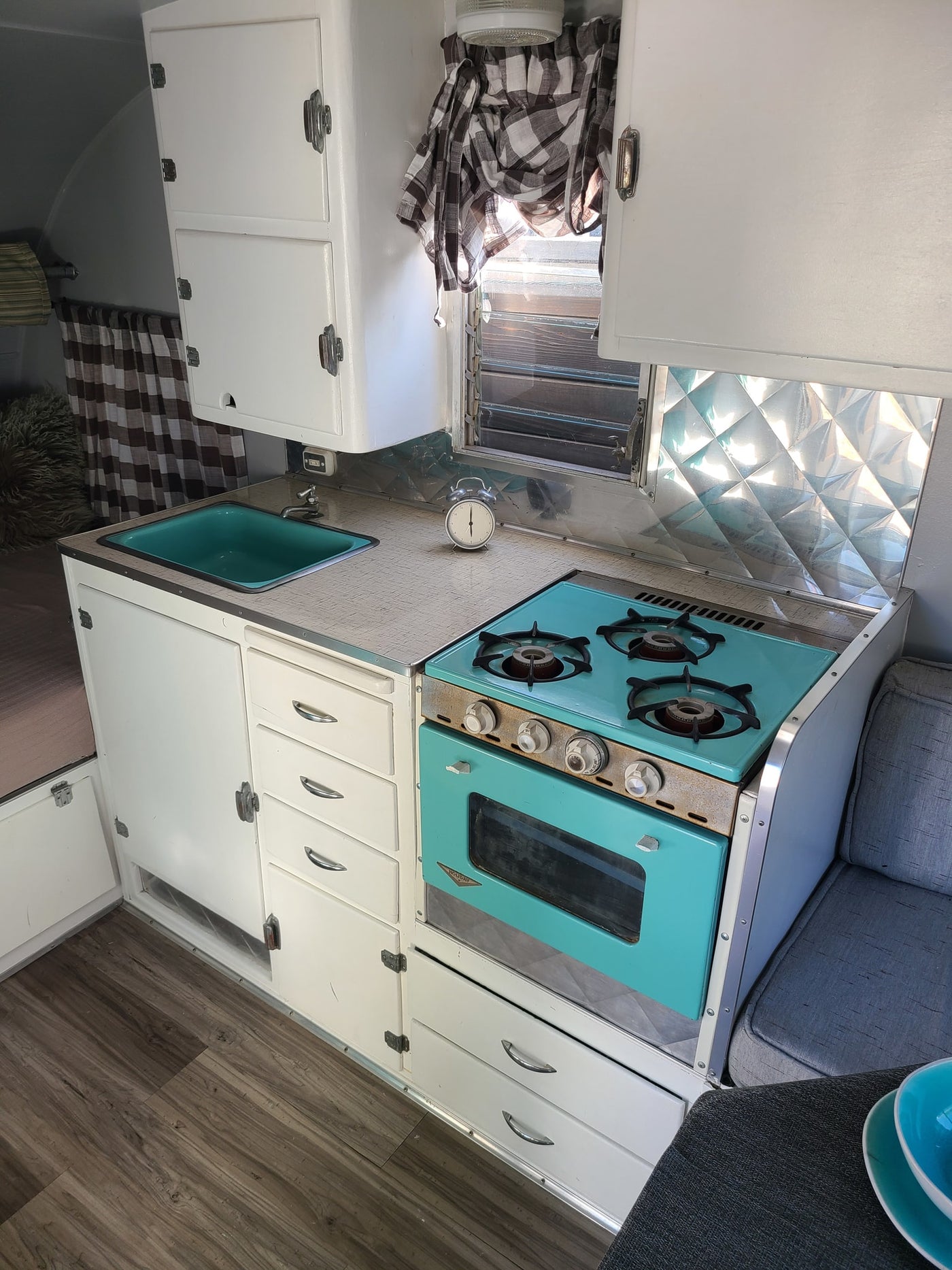 Explore this charming vintage RV rental interior with a vibrant teal kitchen, white cabinets, and wood-look flooring. — photo 9