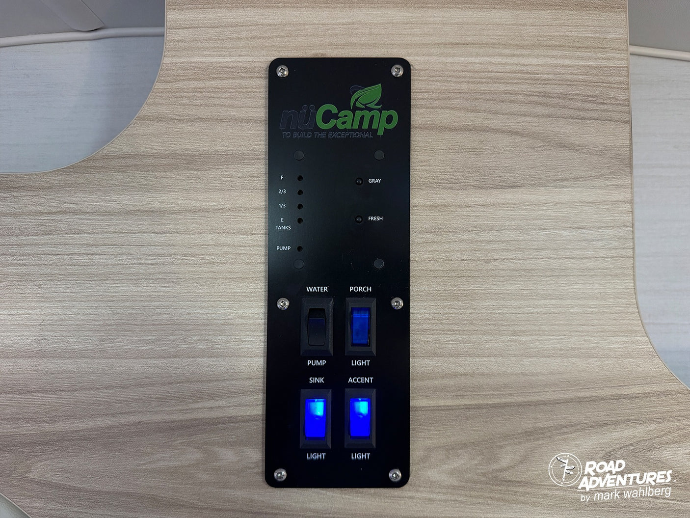 Black nuCamp control panel in an RV rental, showing tank level indicators, water pump, and light switches (porch, sink, accent).