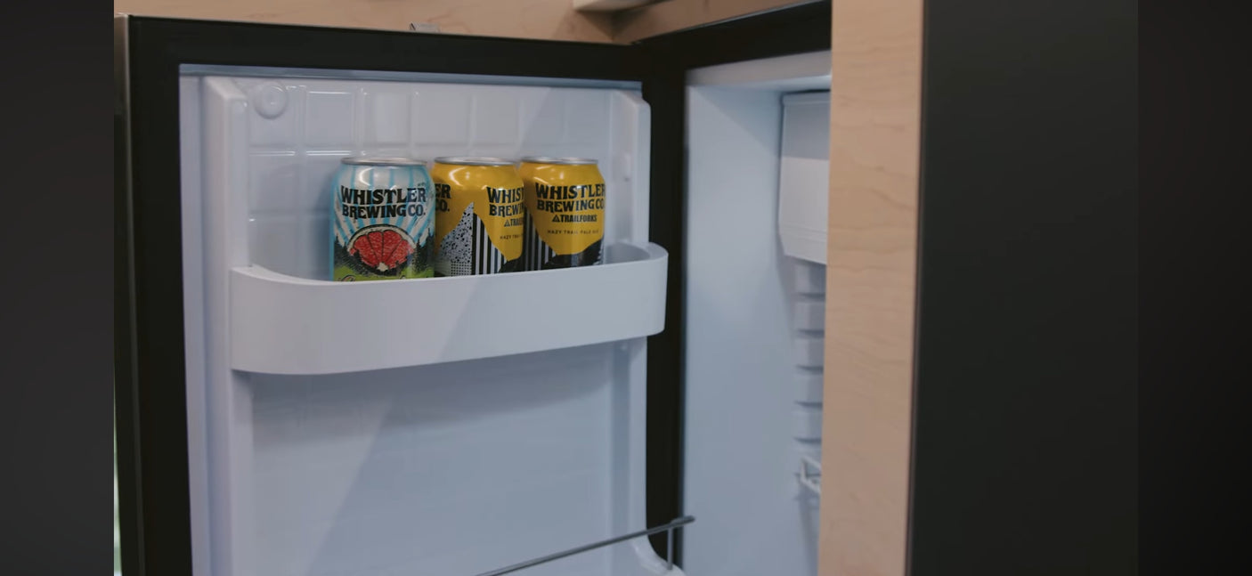 An open mini-fridge in an RV rental, stocked with three cans of Whistler Brewing Co. beer, ready for your road trip.