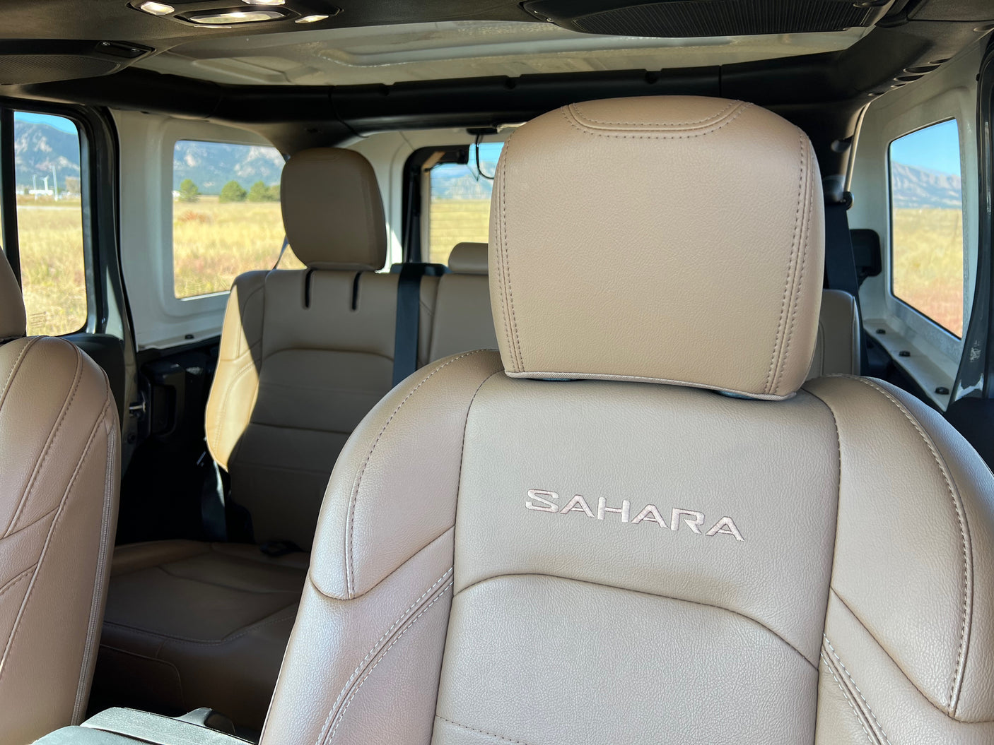Jeep Sahara's tan leather interior, with embroidered logo, inviting for an rv rental road trip through scenic mountains.