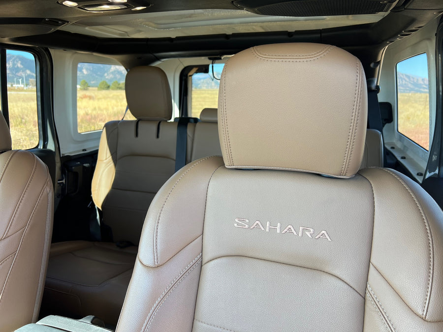 Jeep Sahara's tan leather interior, with embroidered logo, inviting for an rv rental road trip through scenic mountains.