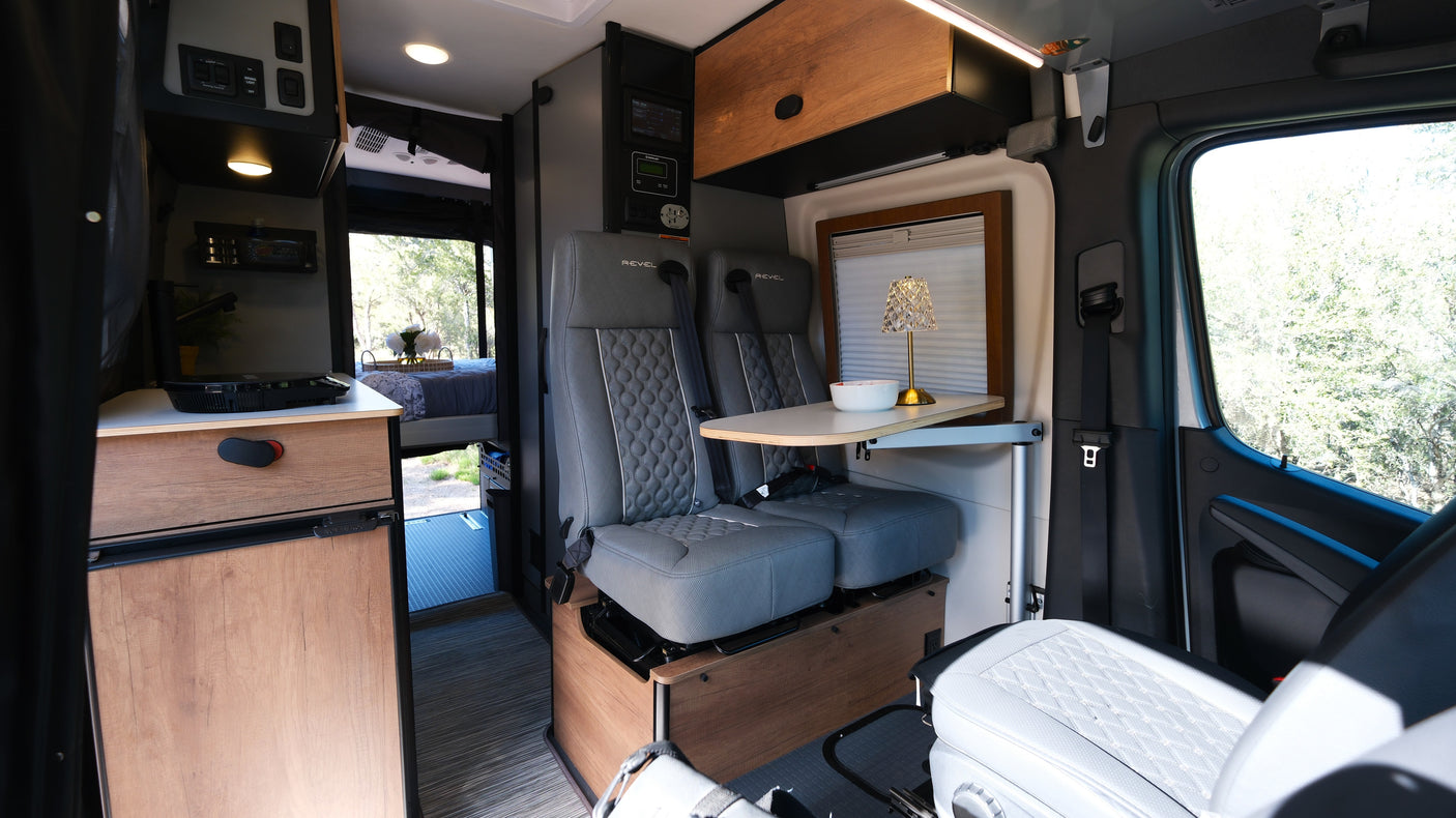 Inside this stylish rv rental: swivel seats, dining table, controls, kitchen unit, and a comfortable bed. Ready for travel.