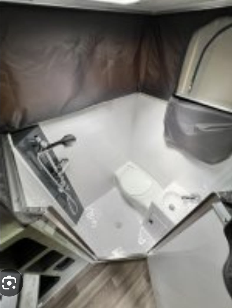 RV rental: Compact bathroom with white shower, toilet, & sink. Dark walls indicate pop-top design.