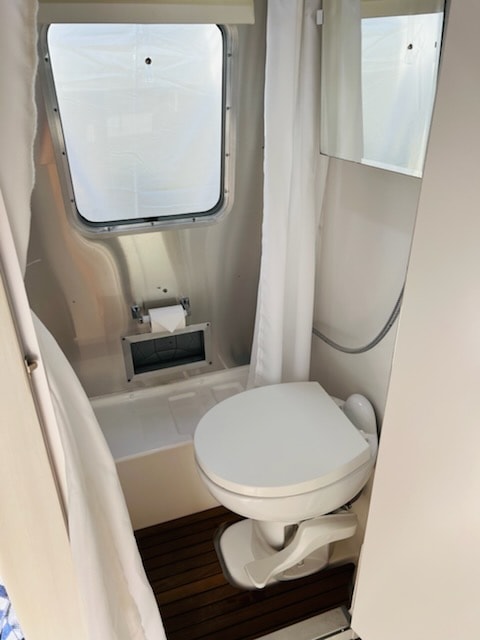 RV rental's compact bathroom shows a white toilet, shower area with curtain, and window for natural light.