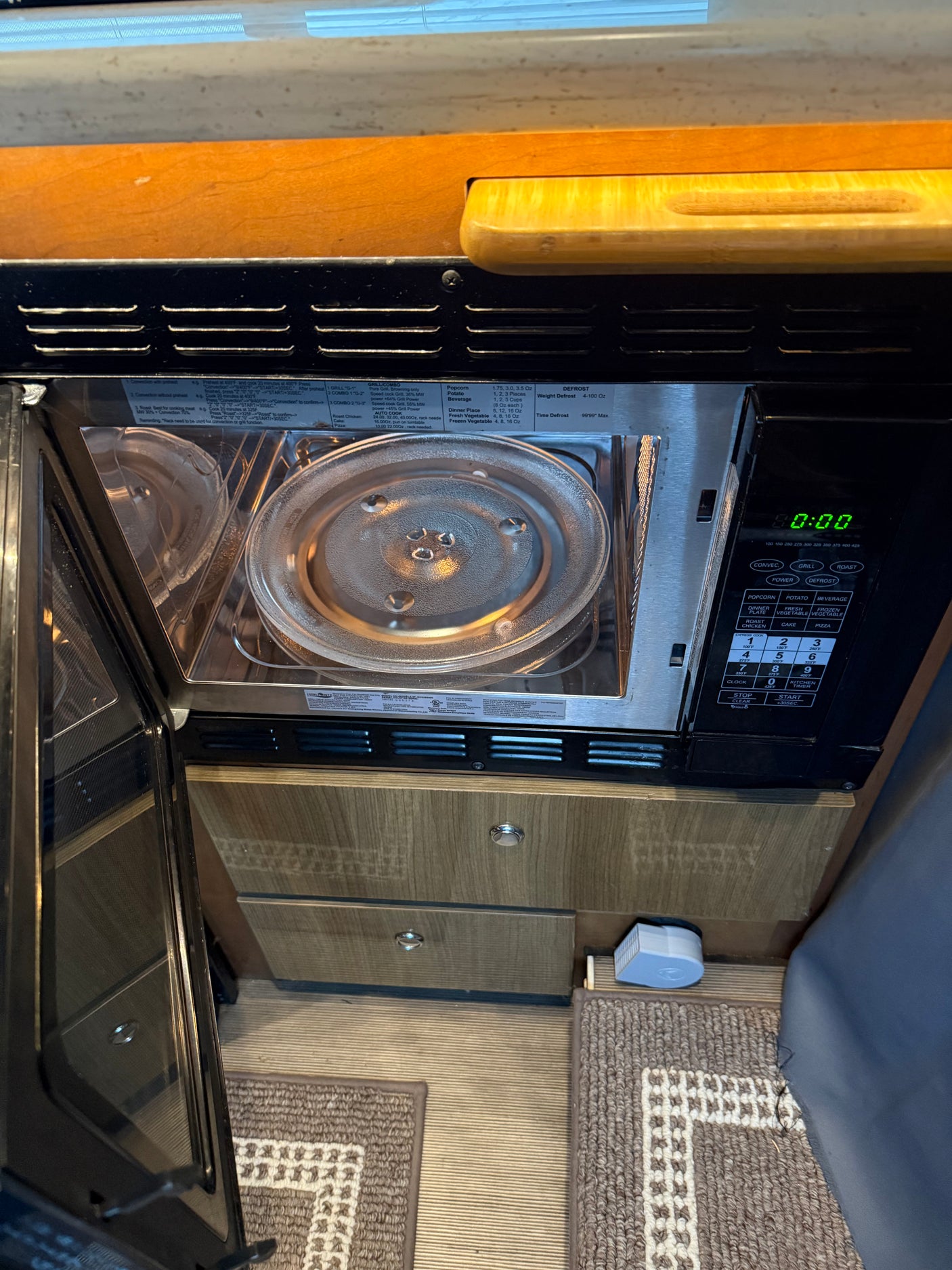 RV rental kitchen: Open microwave showing its interior, glass turntable, and digital controls displaying 0:00 with cooking options.